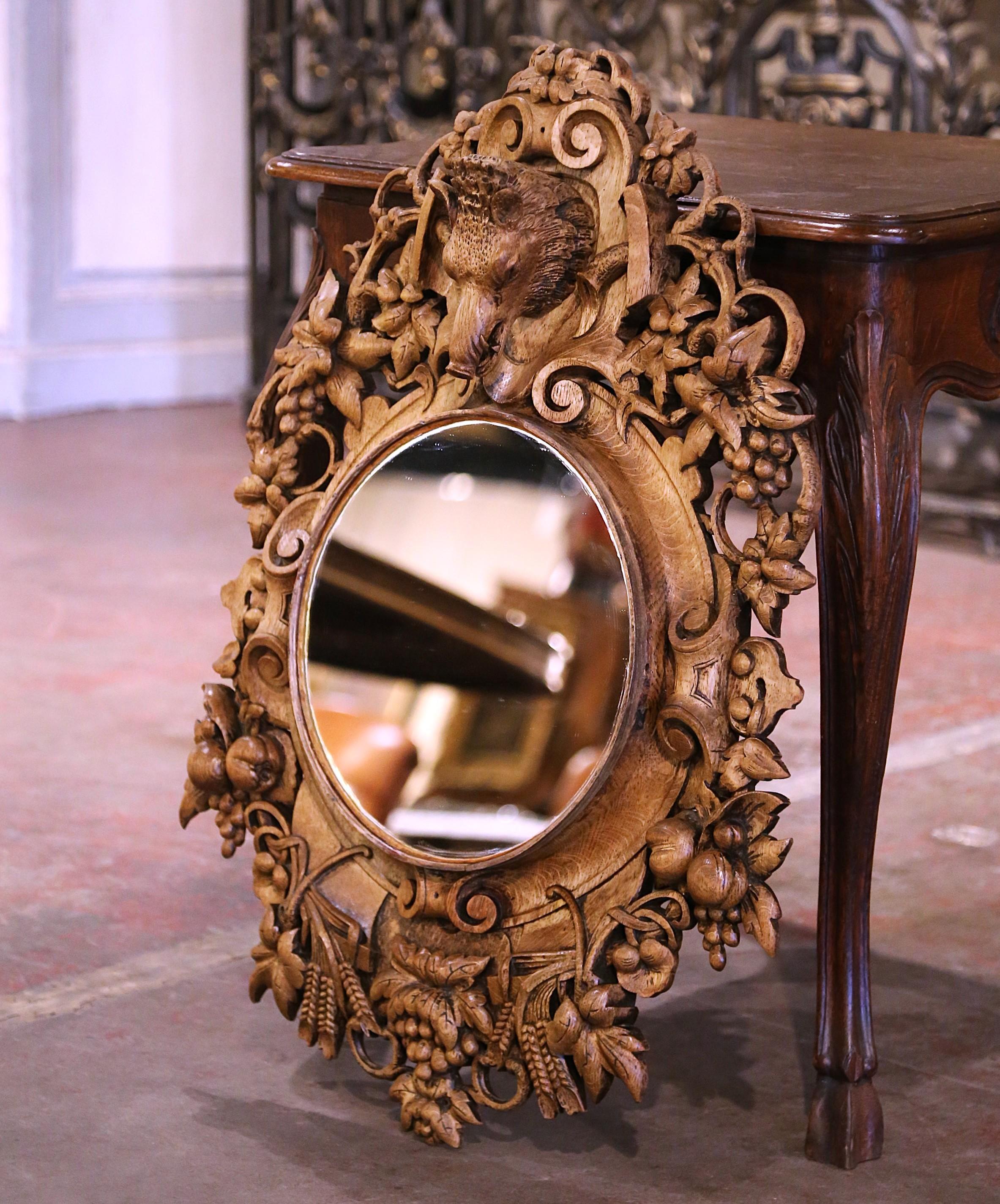 Decorate a study or hallway with this heavily carved antique mirror. Created in France circa 1880 and almost 3 feet tall, the Black Forest frame features a top crest depicting a wild boar's head, surrounded with carved and pierced pendants of fruit