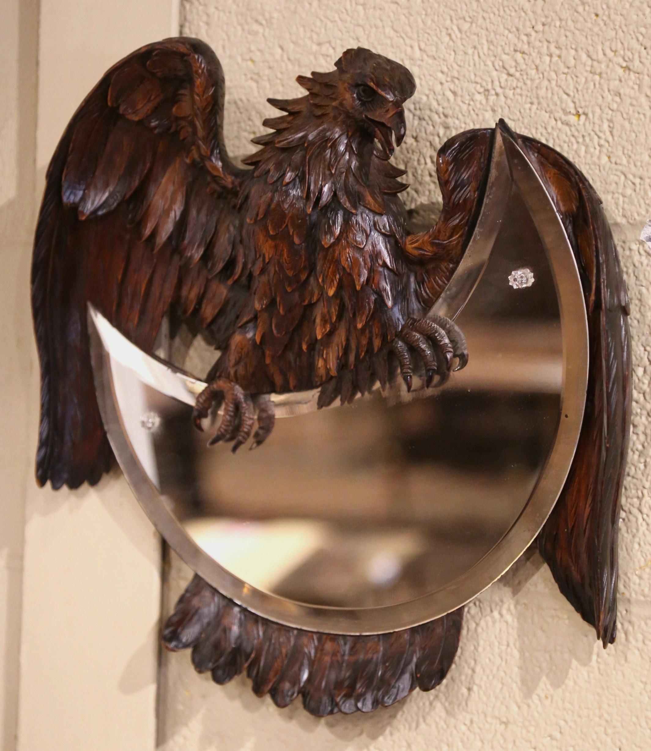 This unusual antique mirror was crafted in the Alps region of France, circa 1880. The whimsical mirror features a large eagle sculpture with wings and tail wrapped around a half moon mirror with beveled mercury glass. The bird features exquisite and