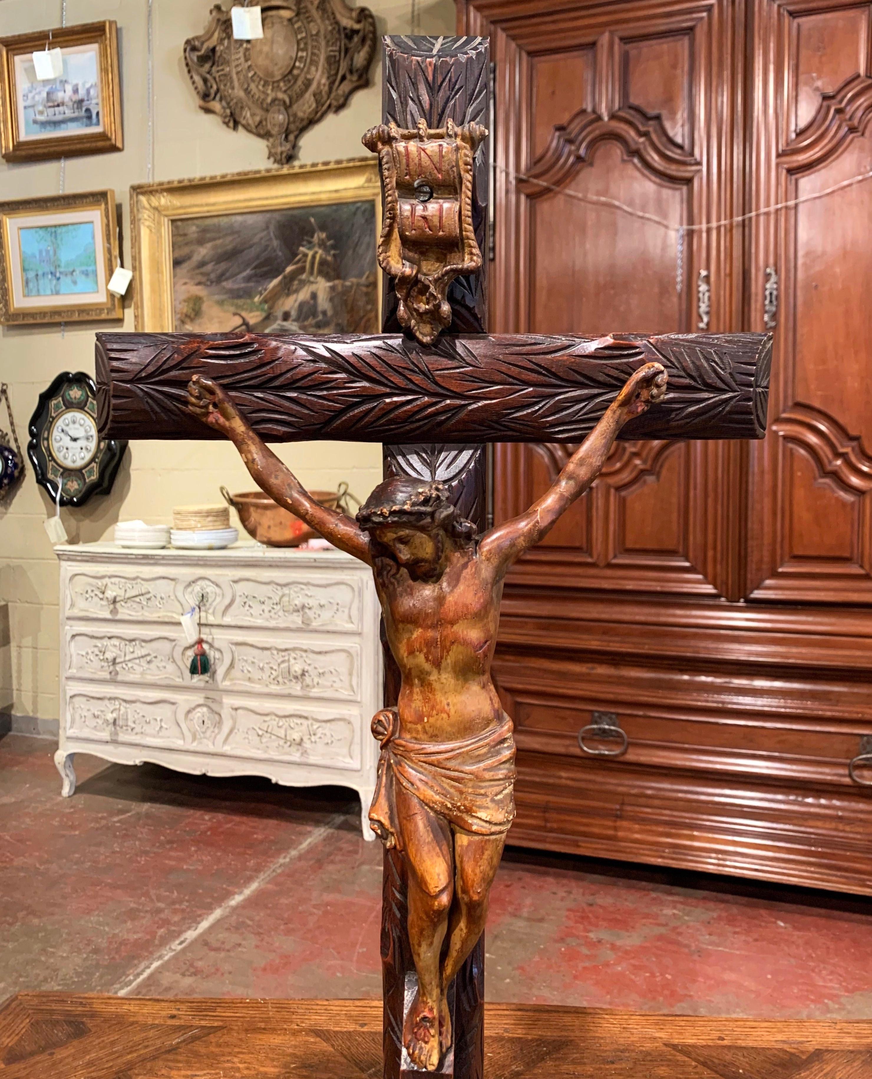 This antique cross was hand carved in France, circa 1870. The intricate crucifix stands on a rocky base and features the Lord nailed on the cross and painted with a polychrome finish. The large religious item is in excellent condition with a rich