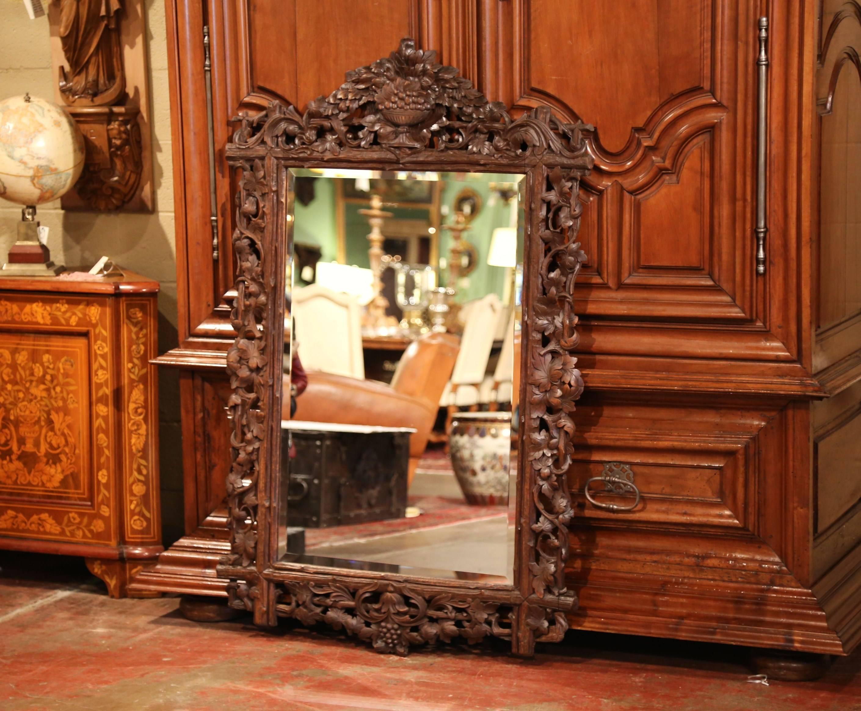 This large antique wall mirror was crafted in the Alps of France, circa 1870. The hand carved fruit wood mirror features a vase full with grapes and leaves at the pediment, with foliage and tree branches all the way around the frame. The impressive,