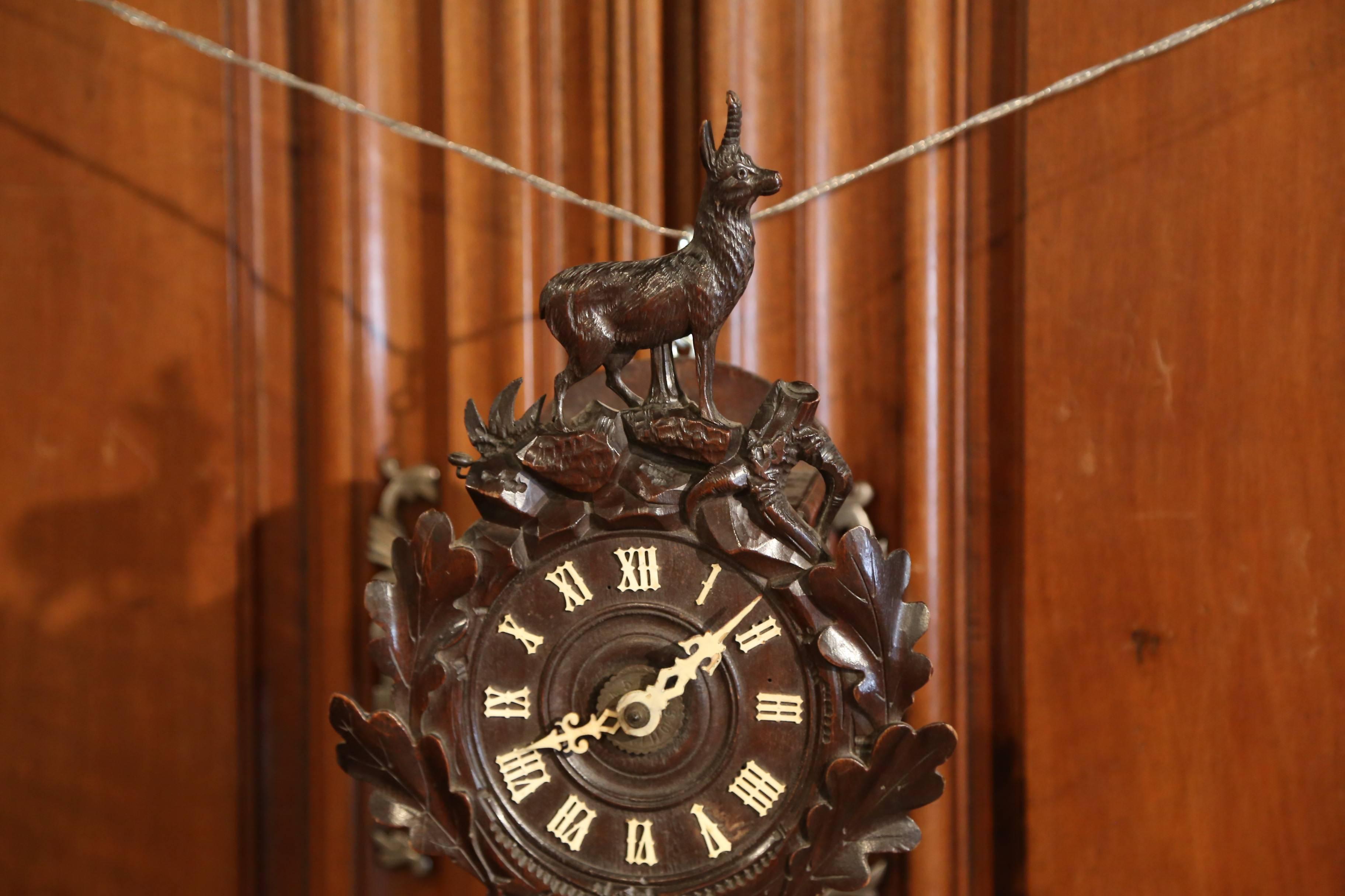Elegant small wall hanging clock from the Alps mountains of France; crafted circa 1860, the fruit wood time keeper features a hand carved deer standing on rock at the pediment and foliage around the center clock. The black forest clock is in