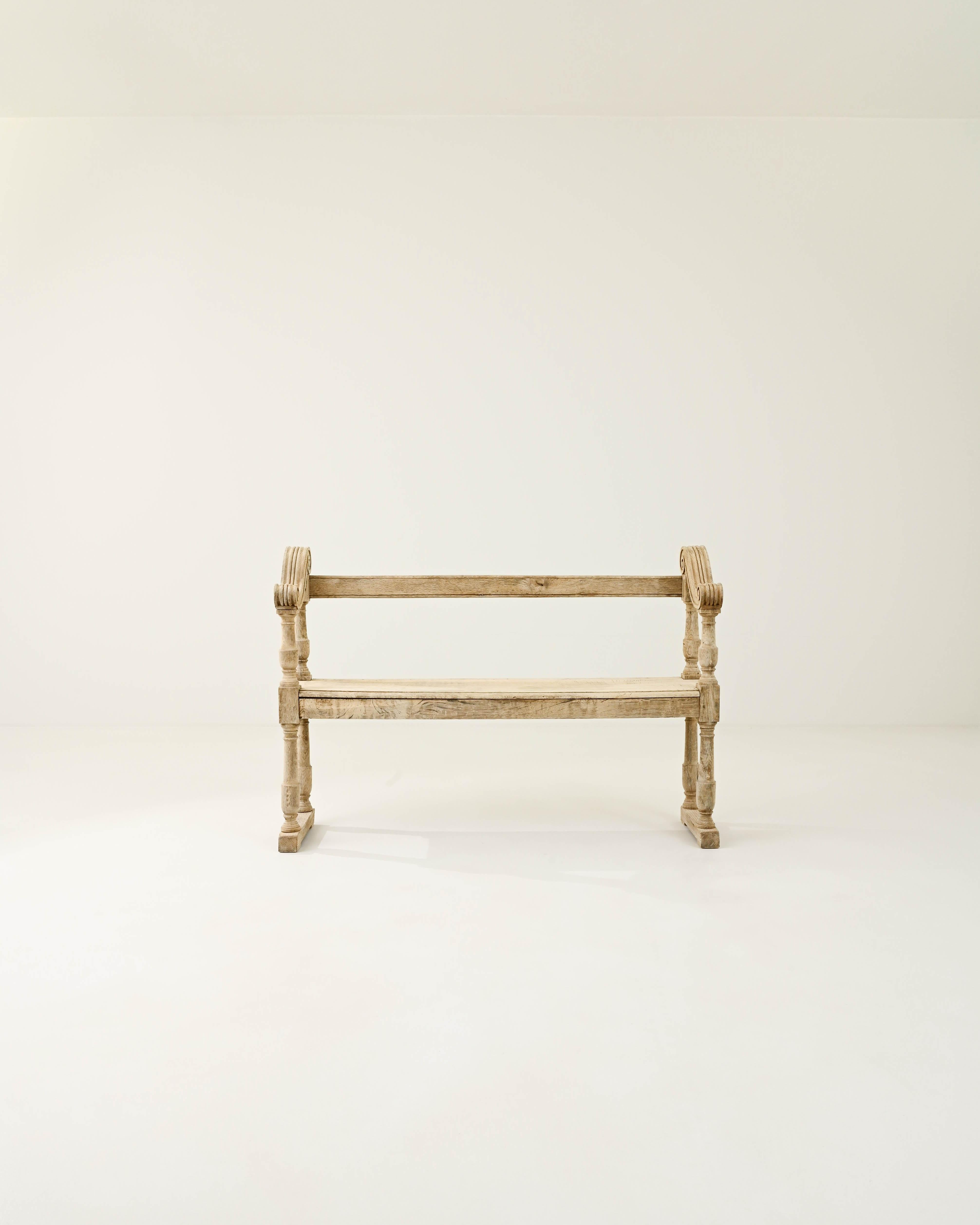 An oak bench from 19th century France. An upright pew-like frame, the sinuous slope of the armrests– fluted and scrolled– lends a graceful inflection. The wood has been restored to a natural finish, revealing the fine grain and subtle blush tones of