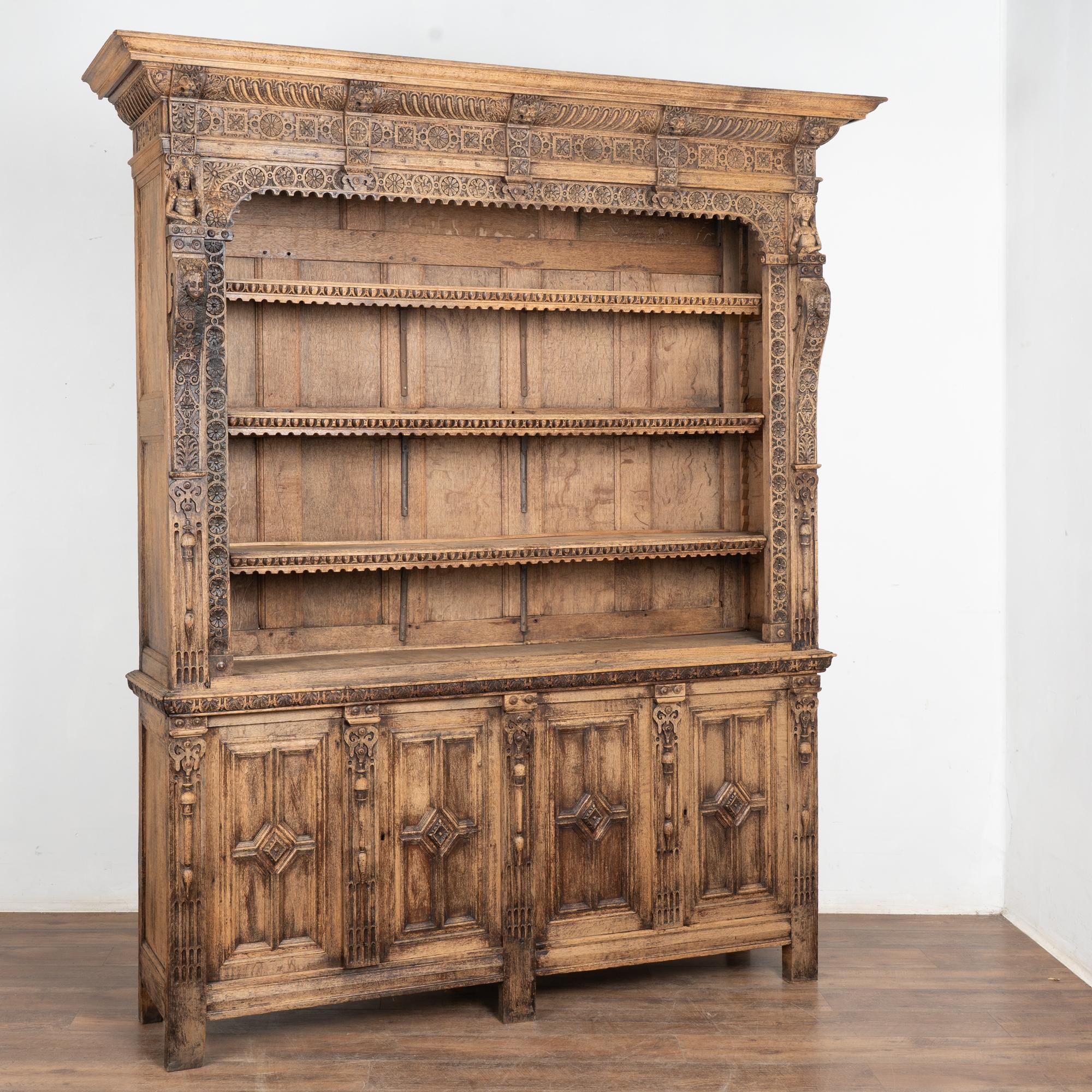 This large bleached oak bookcase is statuesque in size and is impressive with decorative carving including lions, figures, faces, floral medallions and more.
At just over 8' tall, the three shelves allow for great display of books or any collection