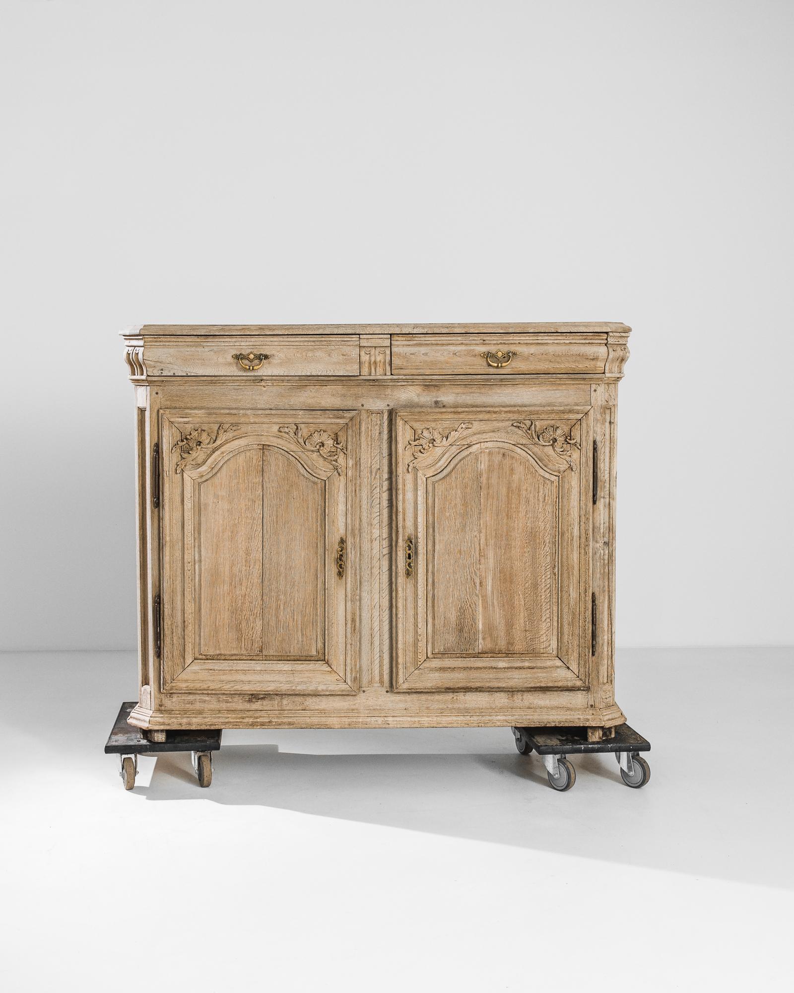 A bleached oak buffet from France, produced circa 1800. A handsome antique buffet, featuring two sliding drawers with brass escutcheons and hanging pulls and a lower, locking double cabinet. In line with the revolutionary spirit of the age bringing
