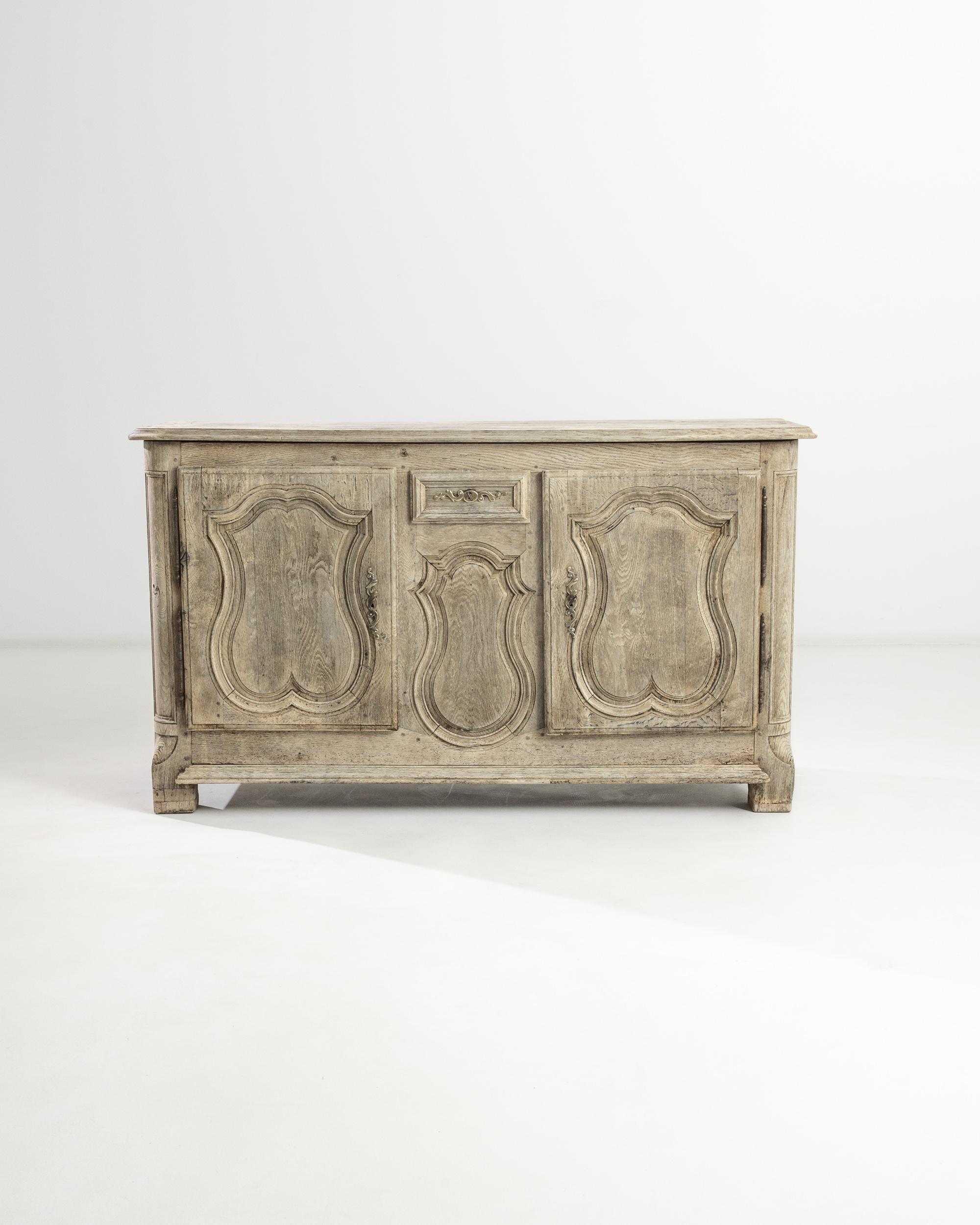 A bleached oak buffet from France, produced during the 19th Century. Bulbous forms etched in relief resemble kissing lips, creating a warm facade for this antique buffet. Featuring two locking cabinet doors and a locking, sliding drawer above a