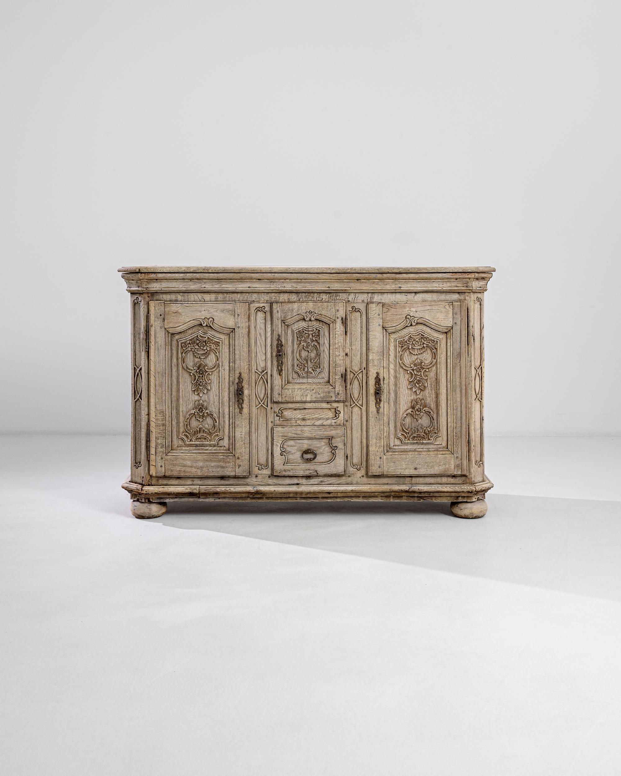 This 19th century French oak buffet boasts elaborate panels with plentiful Baroque flower carvings mirrored on the three raised doors. The piece reveals a strong neoclassical influence, the elegant lines carved in between panels vibrate with a