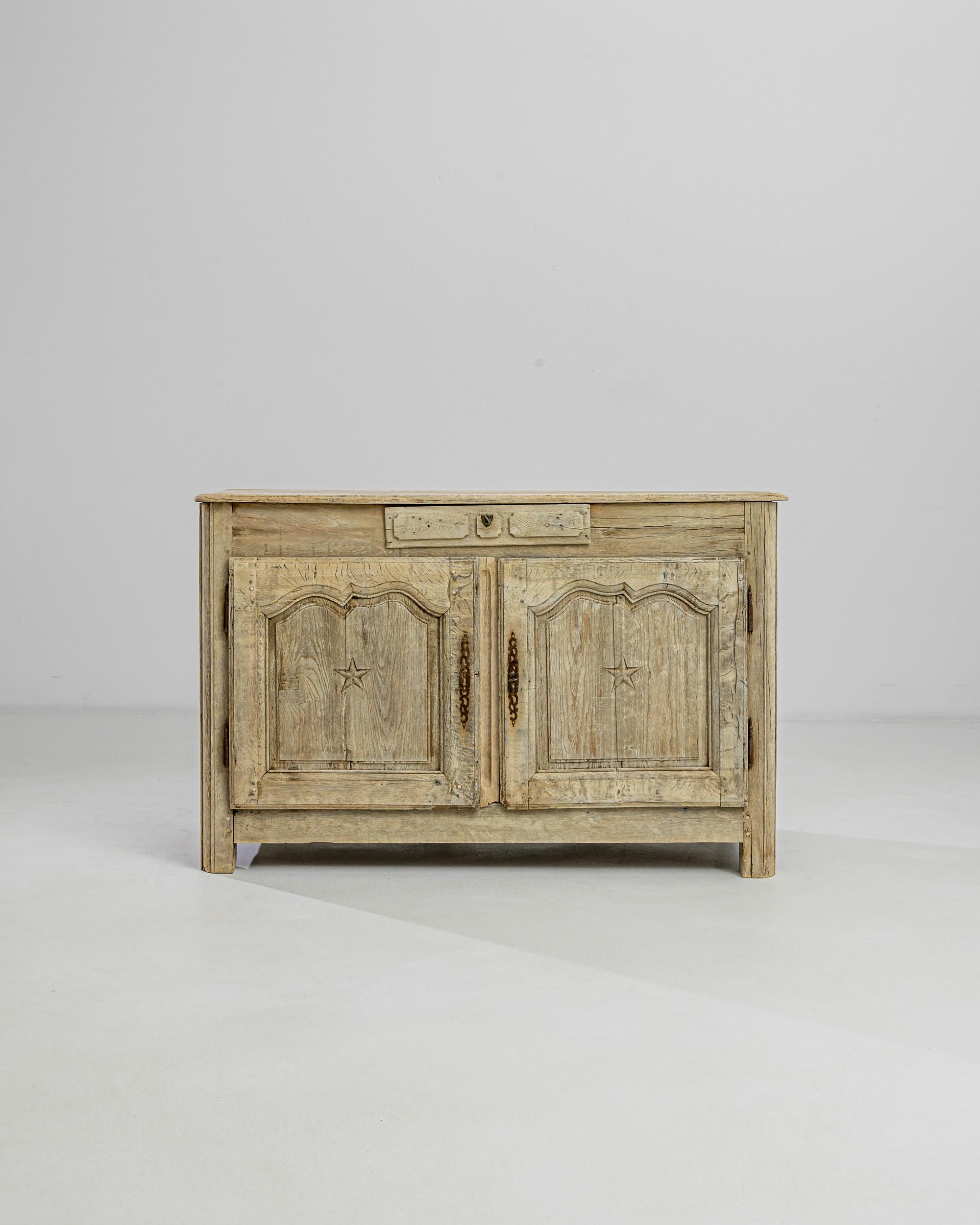 Raised on the sturdy square feet, this 19th century French oak buffet features a single drawer with a crest-shaped lock and two compartments with raised doors adorned with undulating arches and star-carvings. The oxidized patina of the original