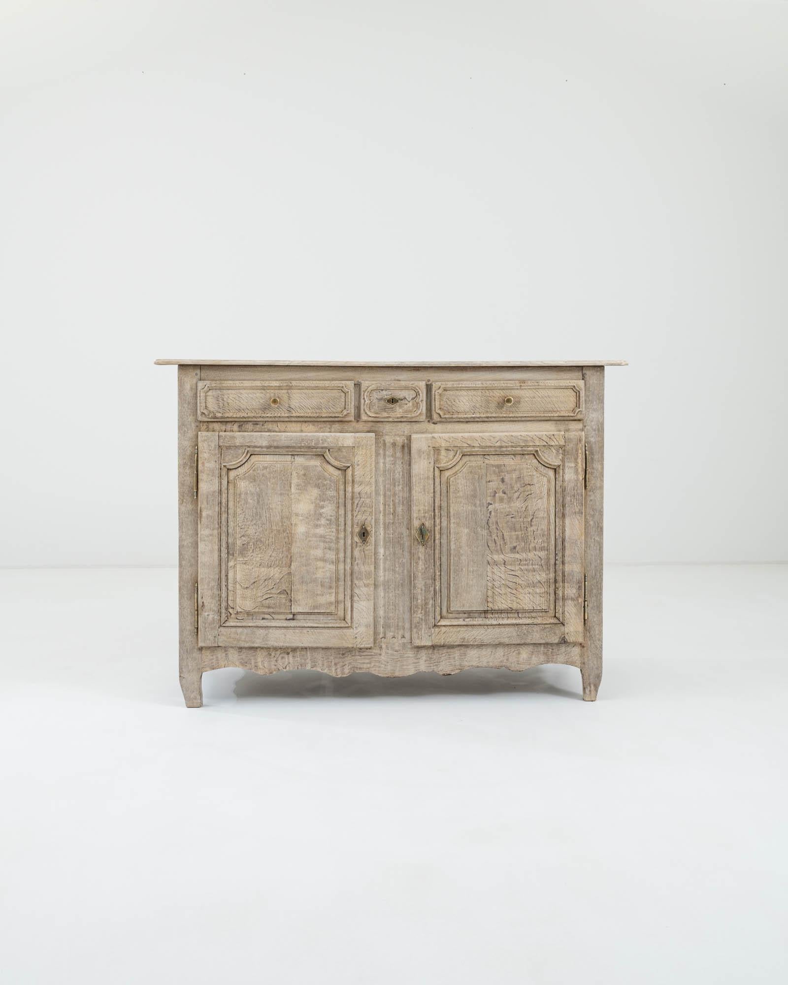 An oak buffet, hand-crafted in France during the 19th century. The blond tone of the bleached wood reveals a graceful rippling grain, punctuating masterfully carved details on the doors and a set of drawers sitting atop them. The slightly curved