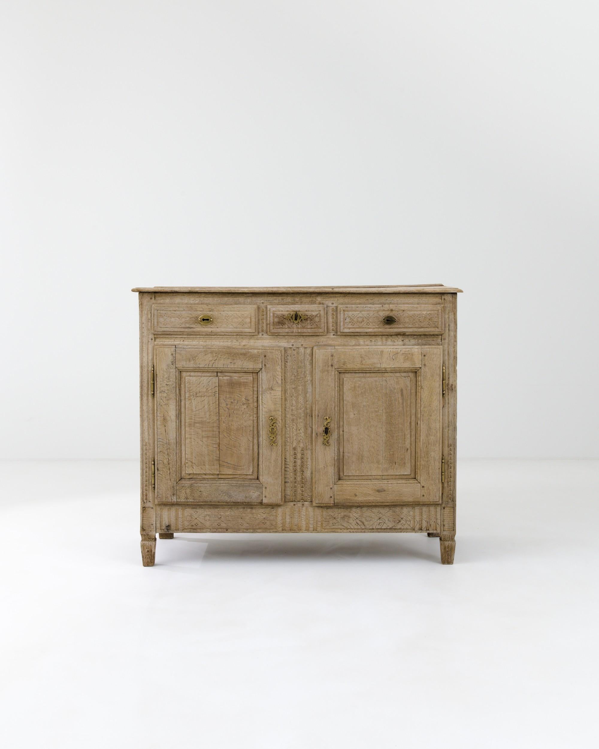 This 19th-century French buffet, handcrafted from fine European oak, flaunts intricate patterns of natural grain combined with subtle carvings decorating the apron. The ornate brass lock pieces on the panel doors of the lower compartments, along