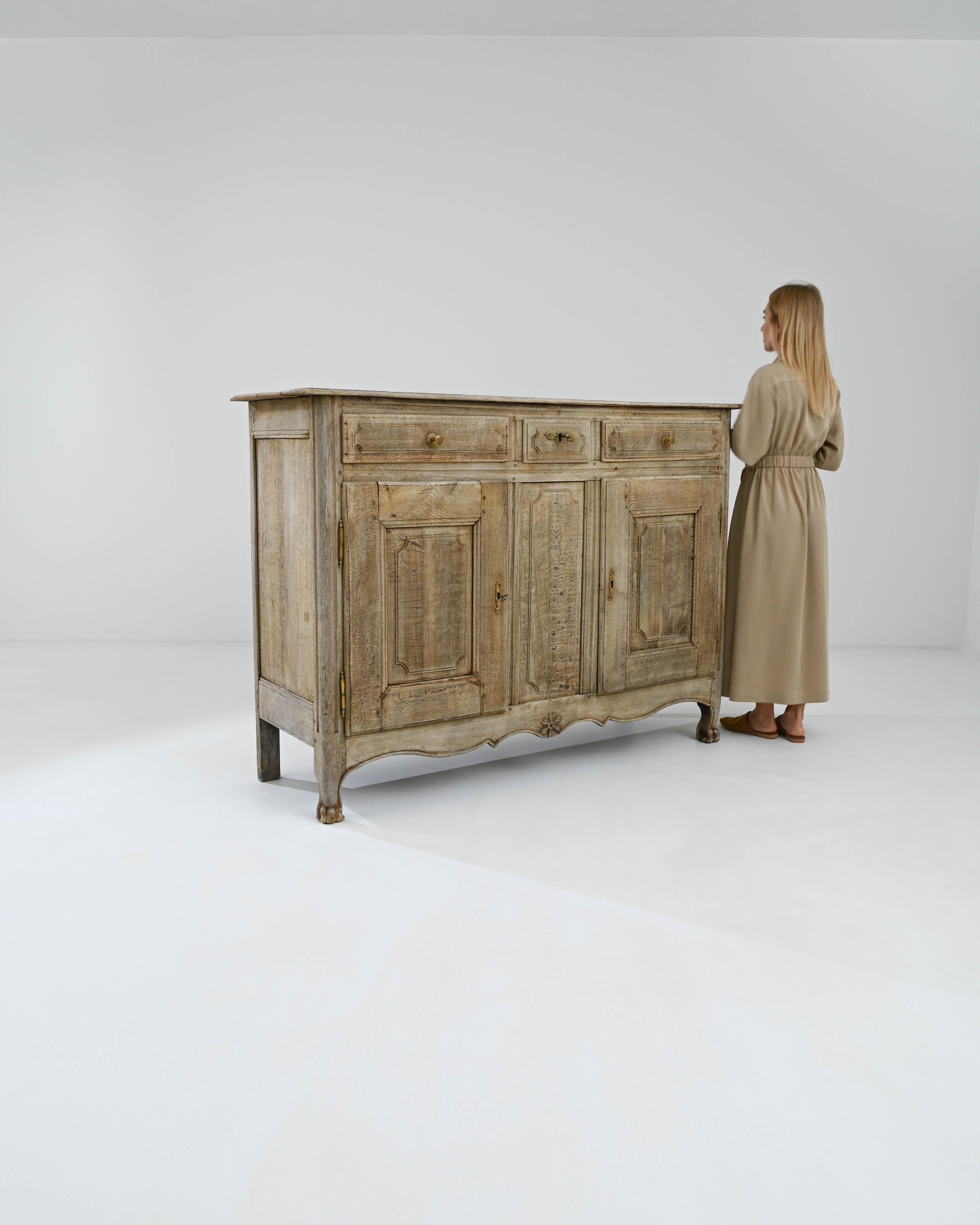 Ce meuble intemporel est un buffet français en chêne blanchi du XIXe siècle qui témoigne du savoir-faire de son époque. Il est couronné de sophistication et comporte trois tiroirs dans sa partie supérieure. Les deux tiroirs latéraux offrent beaucoup