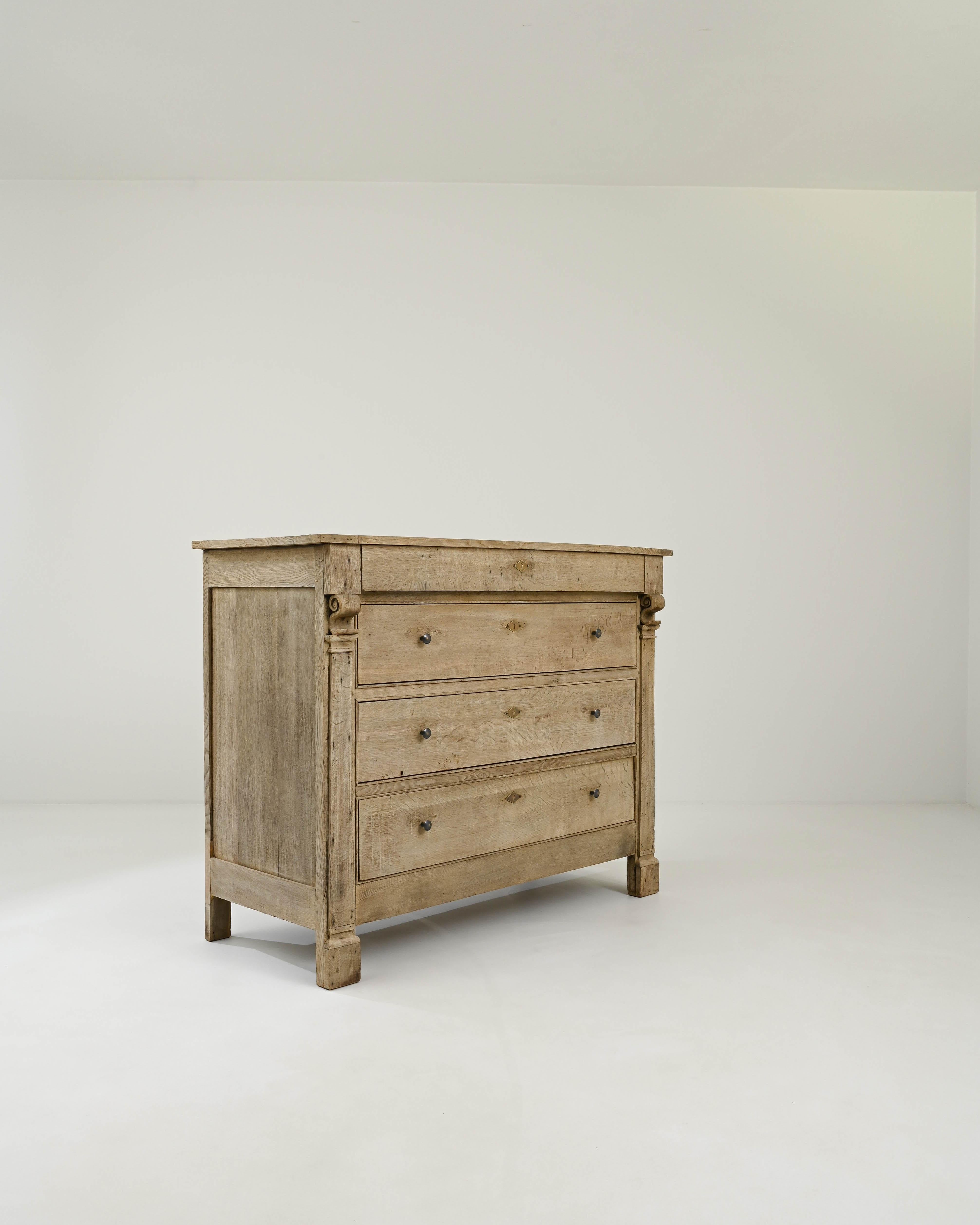The reserved neoclassical elegance shines through the straightforward design of this 19th-century chest of drawers crafted in France. Three spacious drawers are adorned with carved columns topped with skillful scroll carvings. Together with the