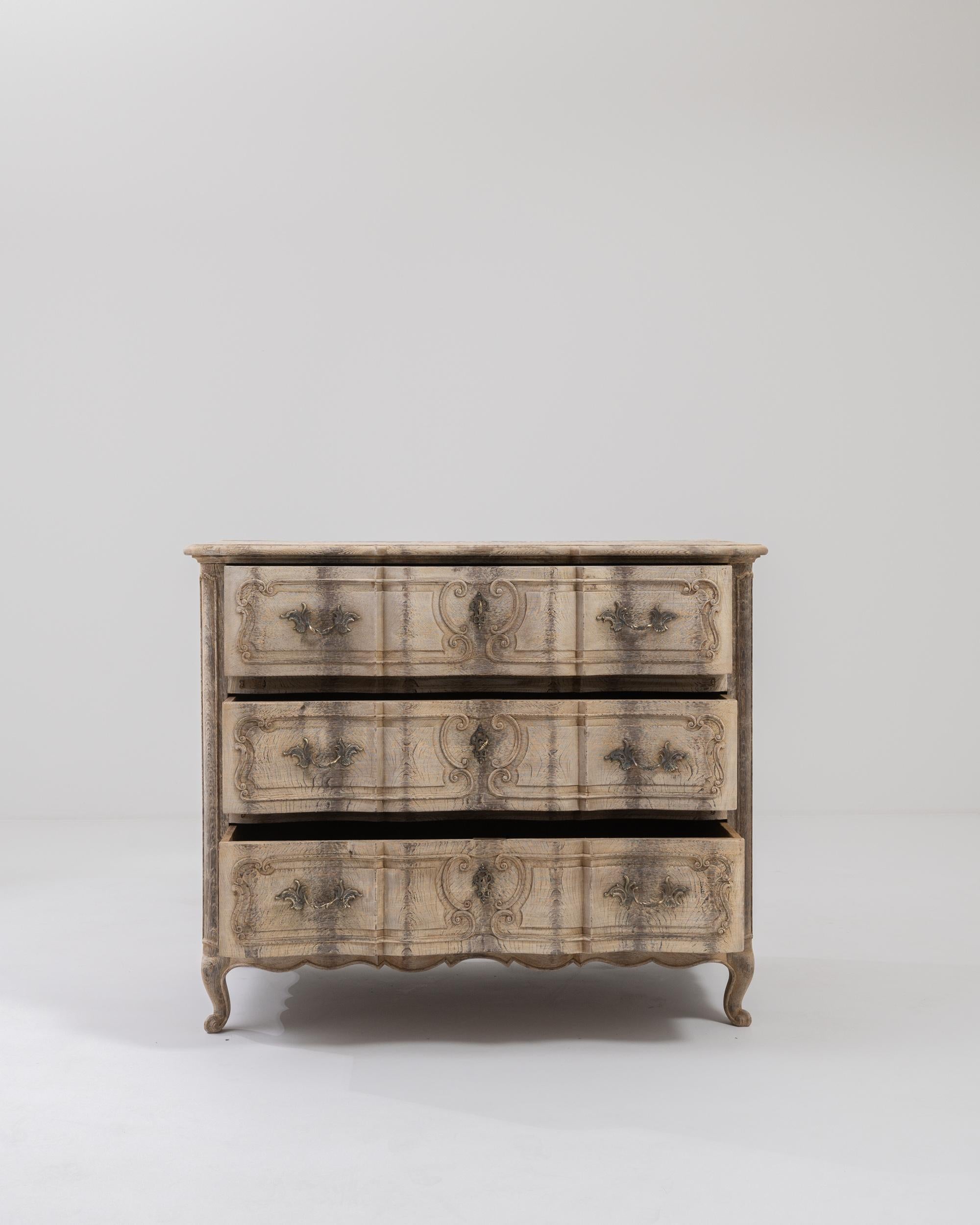 Step into the refined elegance of the 19th Century French Bleached Oak Chest of Drawers, a masterpiece in the exquisite style of Louis XV. This enchanting piece features three drawers adorned with lavish ornate details, showcasing the meticulous