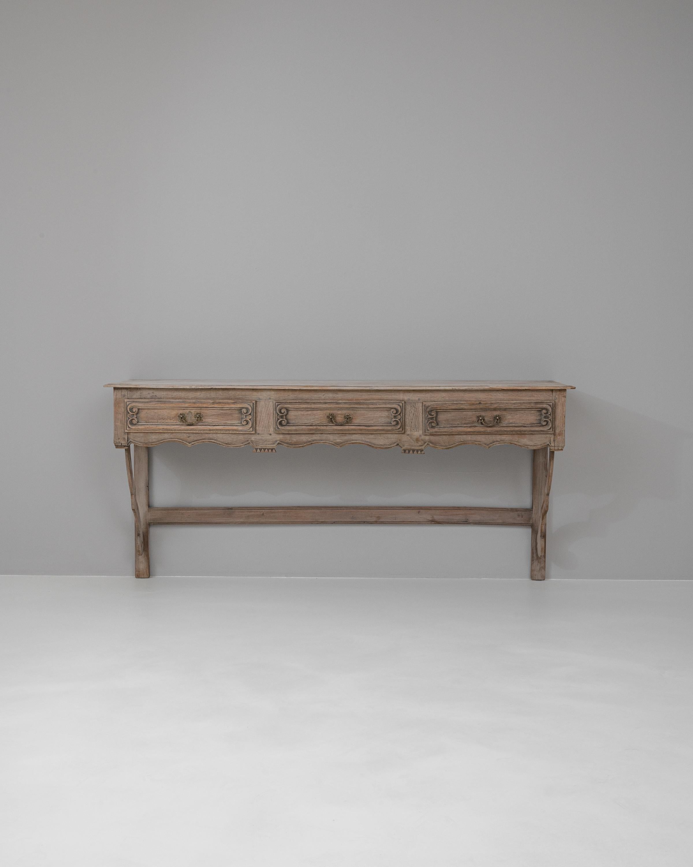 Elevate your home with the refined elegance of this 19th Century French Bleached Oak Console Table. This piece exudes a quiet sophistication with its gracefully carved silhouette and the soft, sun-kissed hues of bleached oak. The twin drawers are