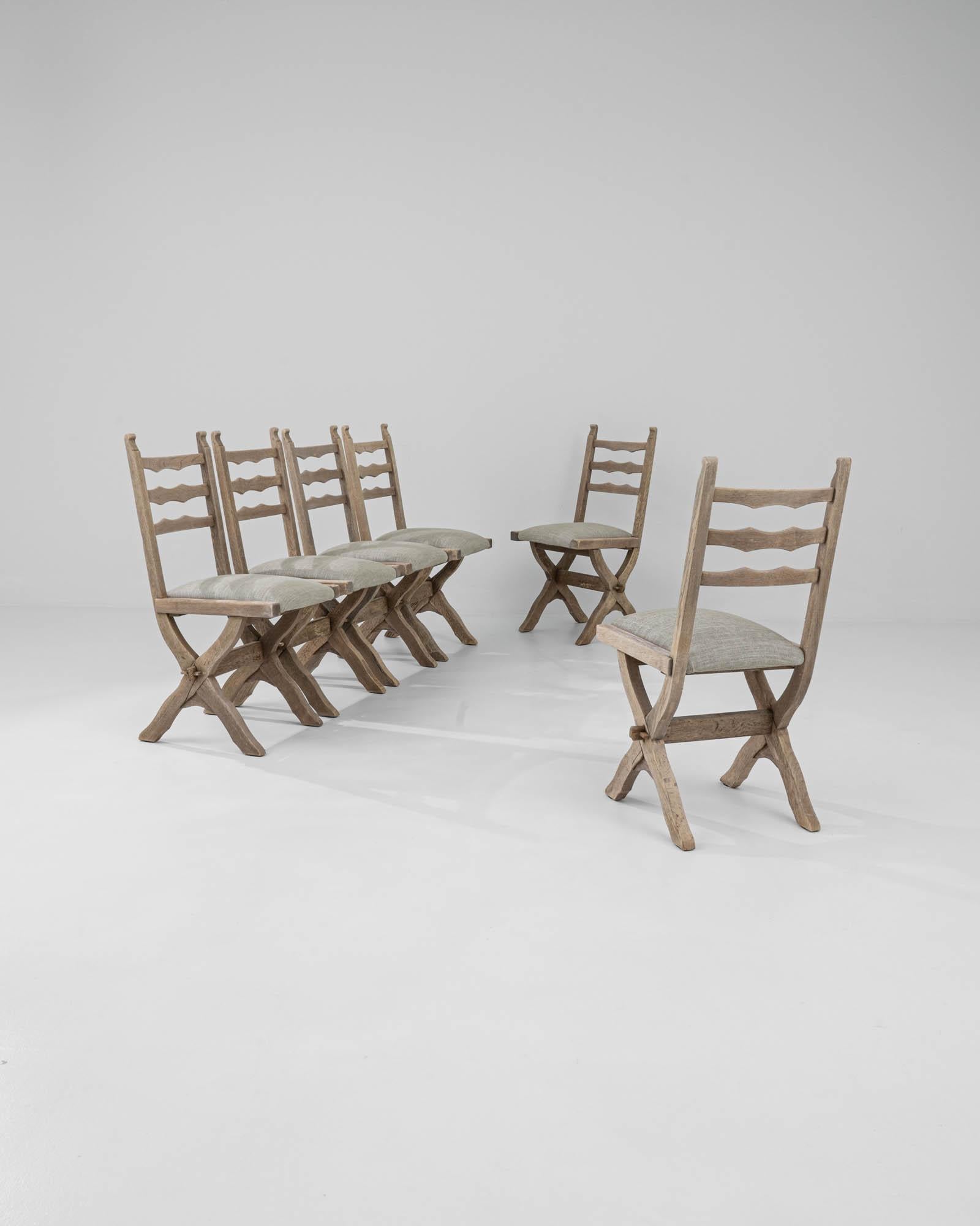 Made in 19th-century France, this set of six oak dining chairs boasts expert woodwork, featuring a beautifully carved X-shaped base and comfortable ladder backs with wavy slats that echo the slight curve of the legs, giving them a rustic touch. The