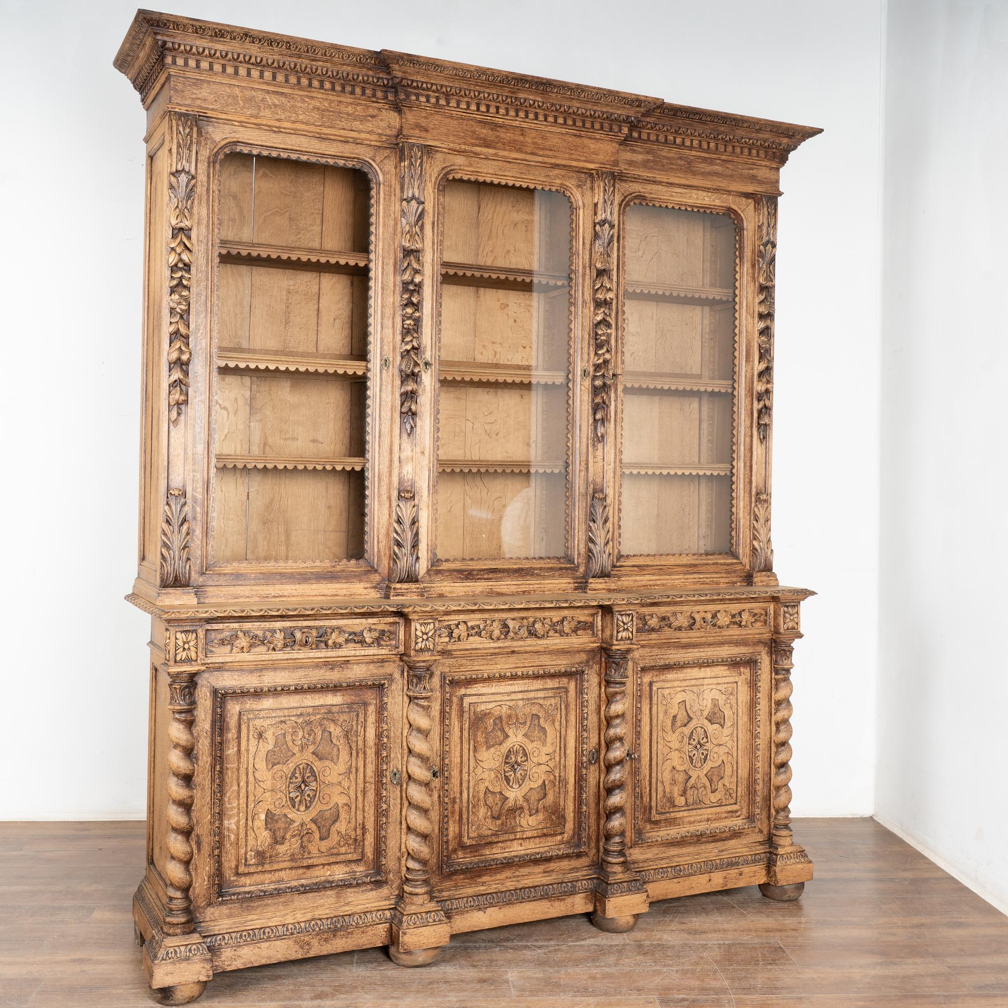 Cette grande bibliothèque en chêne blanchi est de taille statuaire et est impressionnante avec ses panneaux sculptés, ses tiroirs, sa couronne, ses colonnes tournées et bien plus encore.
D'une hauteur d'un peu plus de 8', les 3 portes vitrées