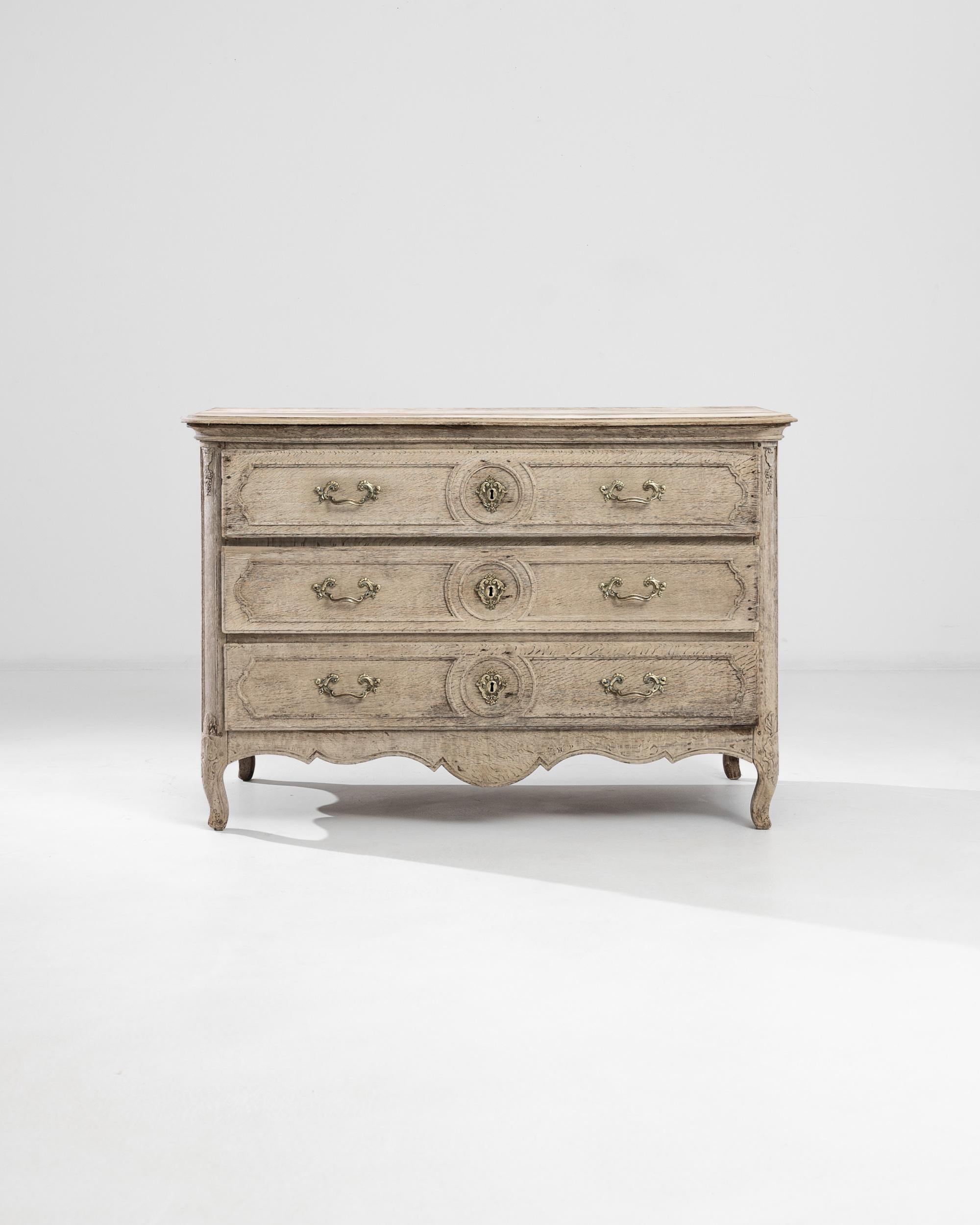 A bleached oak three-drawer dresser crafted in France in the 19th century. From the cabriole legs and scalloped skirt to the panel carvings and molded top, this antique chest of drawers flaunts a dainty neoclassical silhouette embellished by the