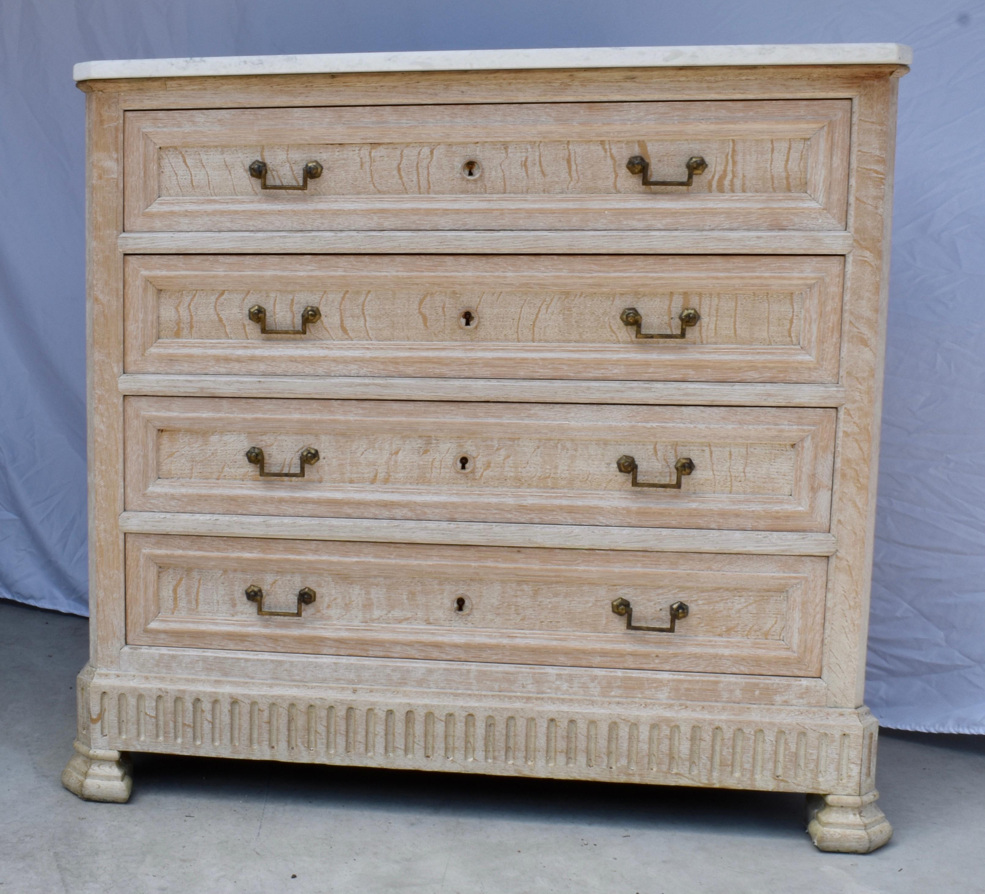 Mid 1800s commode made in France using oak with a white marble top. The commode has a small size and overall linear and simple appearance. The chest features four inset drawers all framed by molding, all showing beautiful hand-made dovetailed