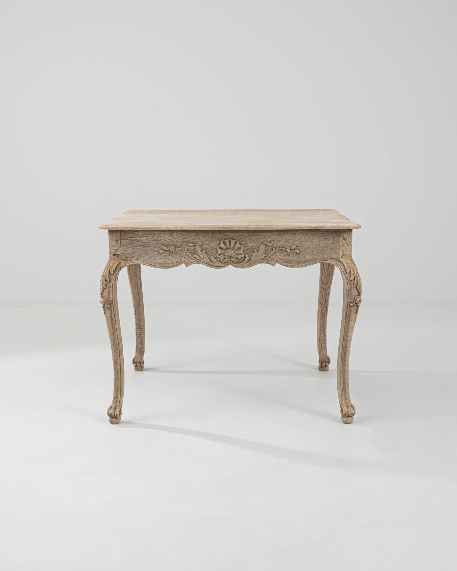 This oak side table was made in 19th-century France. A smooth tabletop with subtly carved edges rests atop an ornate base — the scalloped apron adorned with exquisite floral and foliate carvings, mirrored in the graceful curves of the cabriole legs,