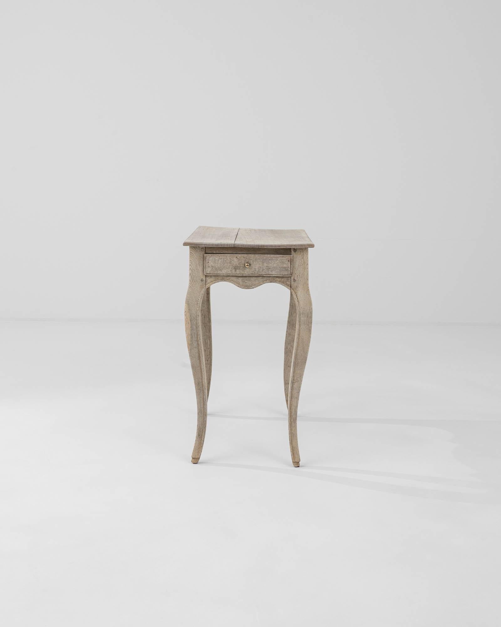 An antique bleached oak table from France with distinctive curved legs. Stylish and practical with a versatile shape, four limbs stretch to support the scalloped apron and a softly beveled tabletop. The piece imparts a playful figure – carved hooves