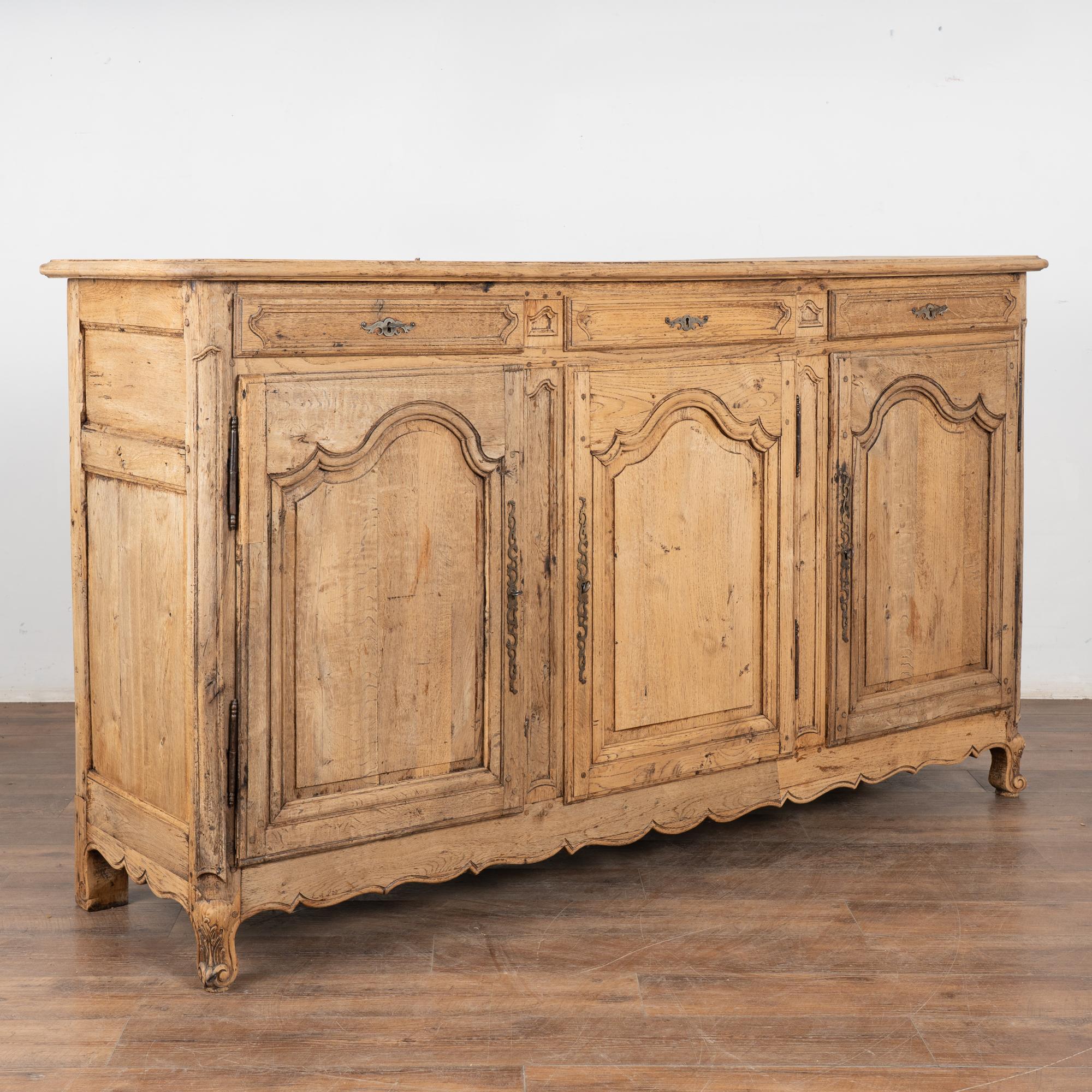 It is the arched paneled doors, scalloped skirt, carved feet and panel detail of the drawers that create the French sense of style seen in this oak sideboard.
The bleached finish gives it a fresh and welcoming look for today's modern home and shows