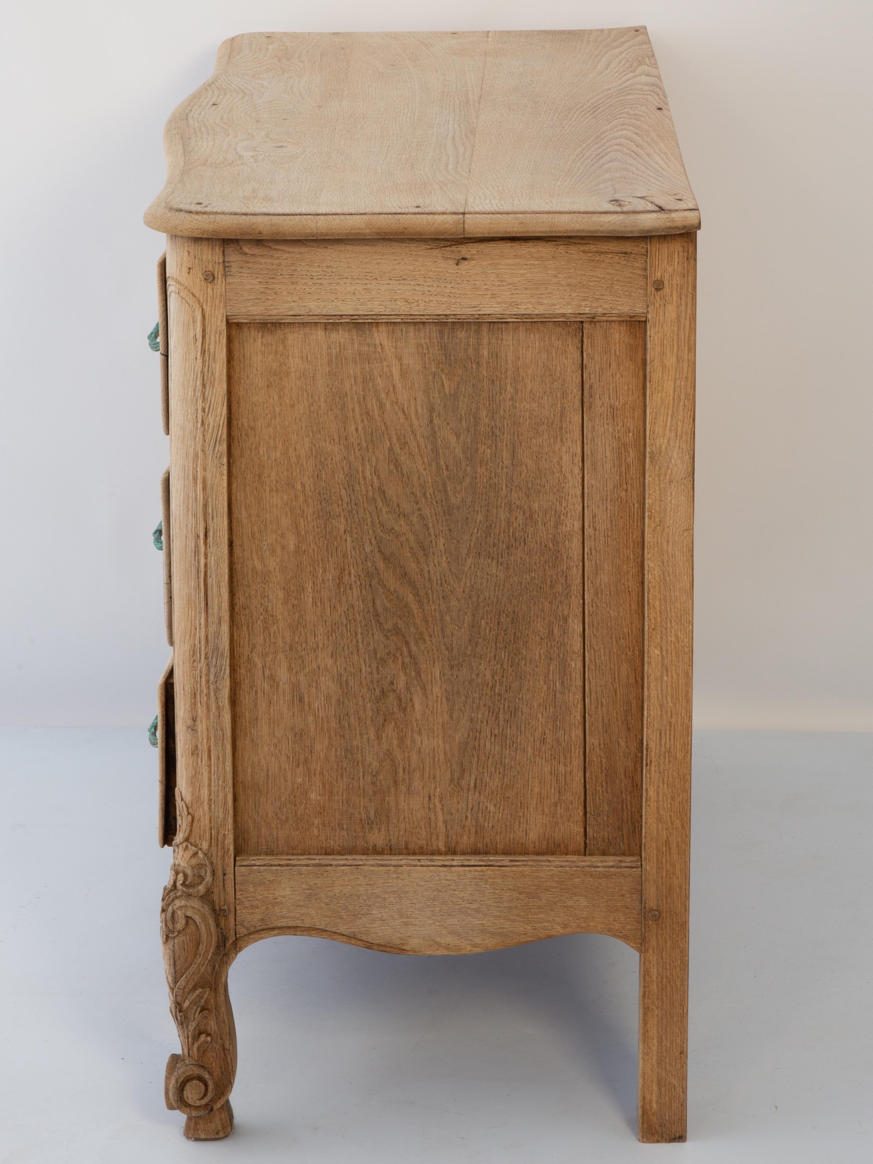 Cómoda de estilo Luis XVI, de roble blanqueado. Su parte superior rectangular moldeada sobre una caja conformada, con tres cajones apilados. Cada uno de los paneles de los cajones, en relieve y acanalados, está centrado por un escudo y flanqueado