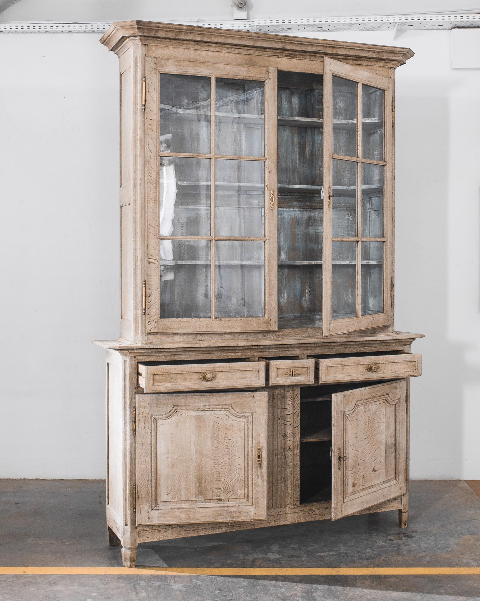 A two part wooden vitrine crafted in France circa 1850. This 103 inch tall antique chest offers plenty of storage space. The upper cupboard with fixed shelves and glazed doors to shed light on inherited family china and silver flatware. The lower