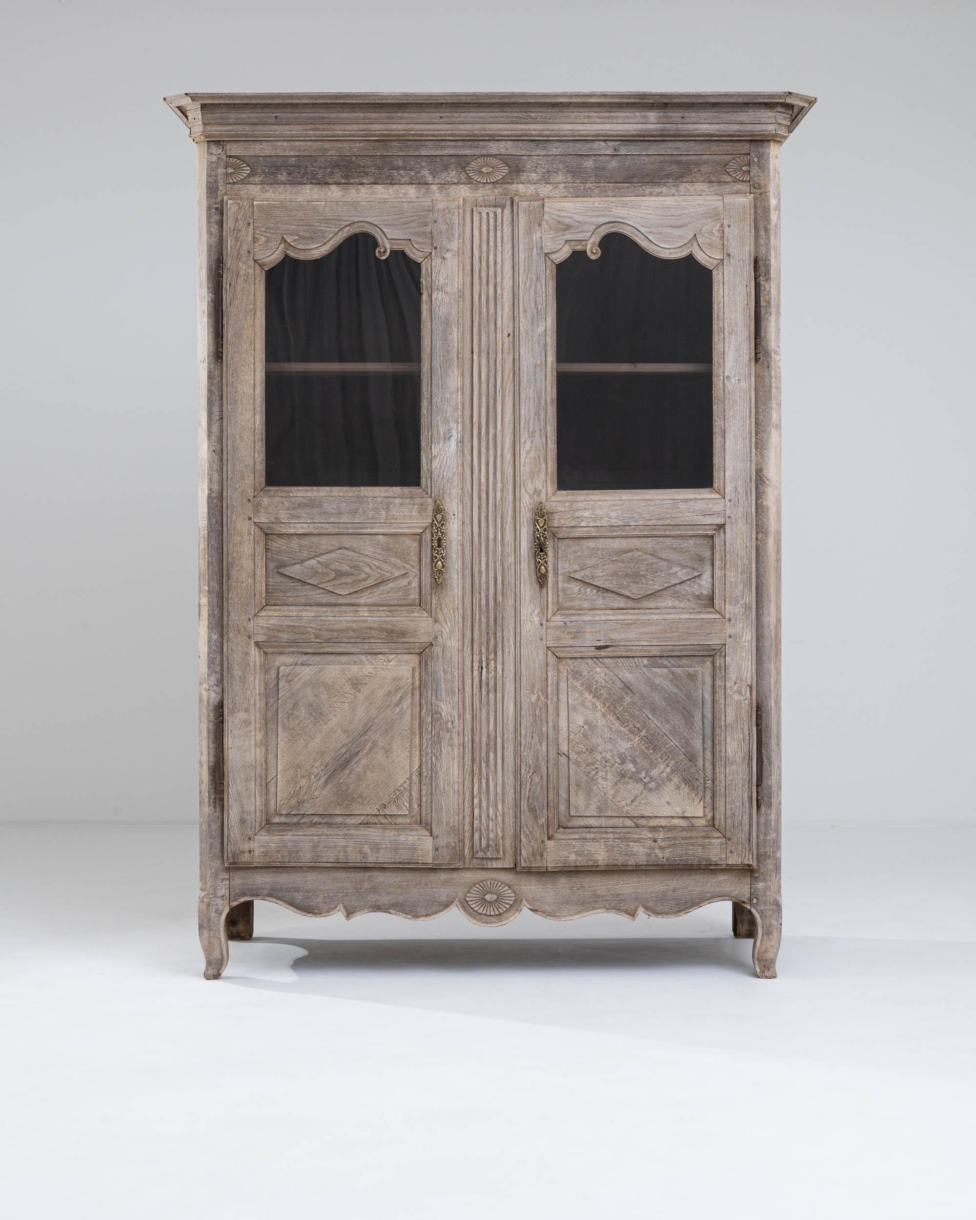 A wooden vitrine made in 19th century France. This lavish vitrine exudes an aura of dignified beauty, featuring two glass paned doors which swing outwards to reveal three shelves. A delicate bleaching process has been applied to the oak,