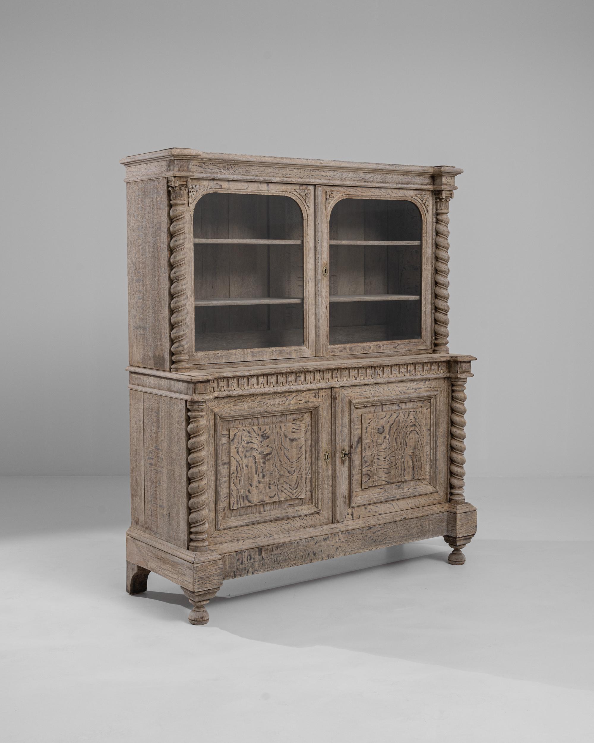 Elevate your living space with the timeless charm of this 19th Century French Bleached Oak Vitrine, where the craftsmanship of a bygone era takes center stage. Barley twist columns, elegantly framing the corners, stand as a testament to the artistry