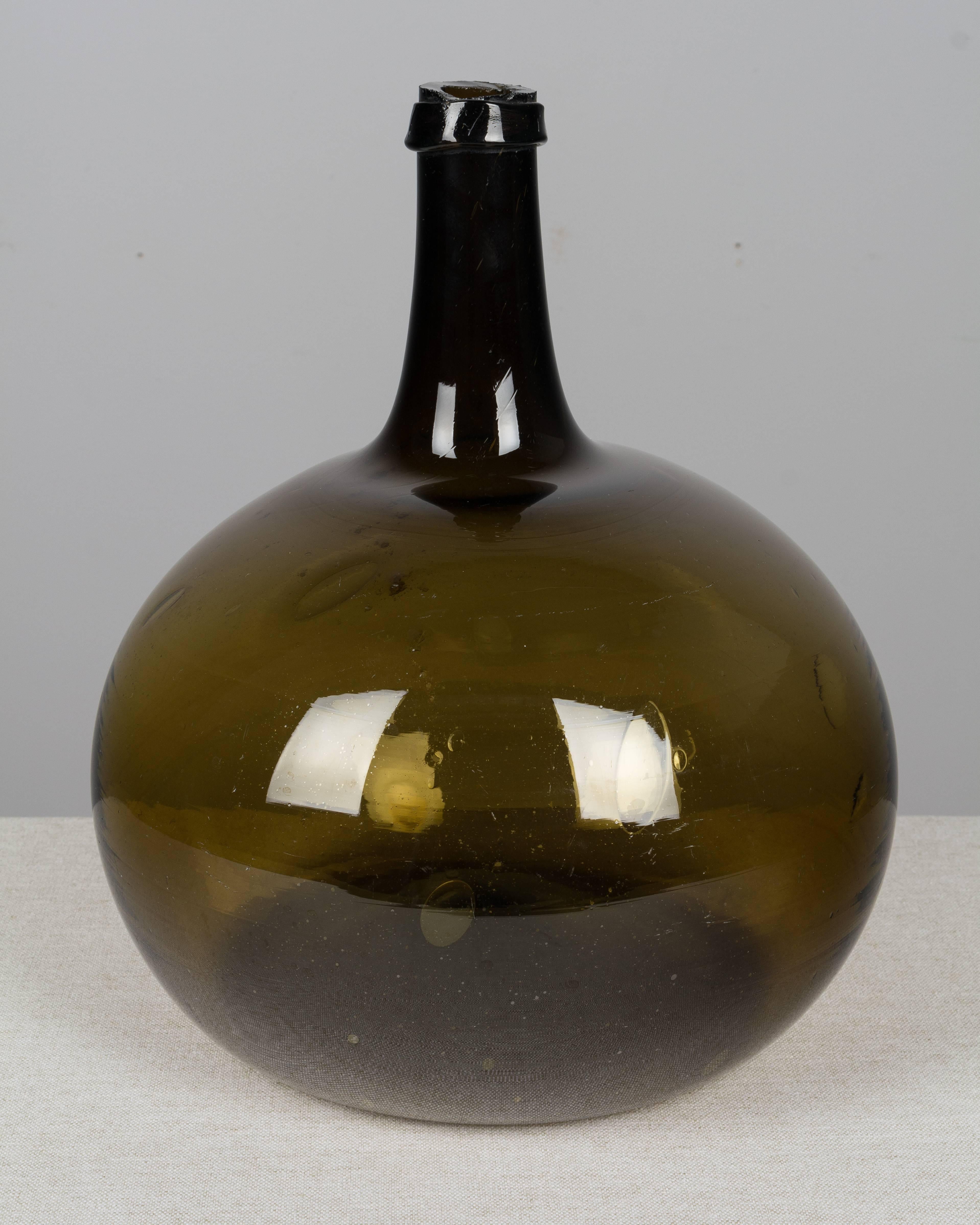A 19th century French globular form demijohn bottle with air bubbles typical of handblown glass.  We have two other bottles in a darker brown color.Please refer to photos for more details. We have a large selection of French antiques at Olivier