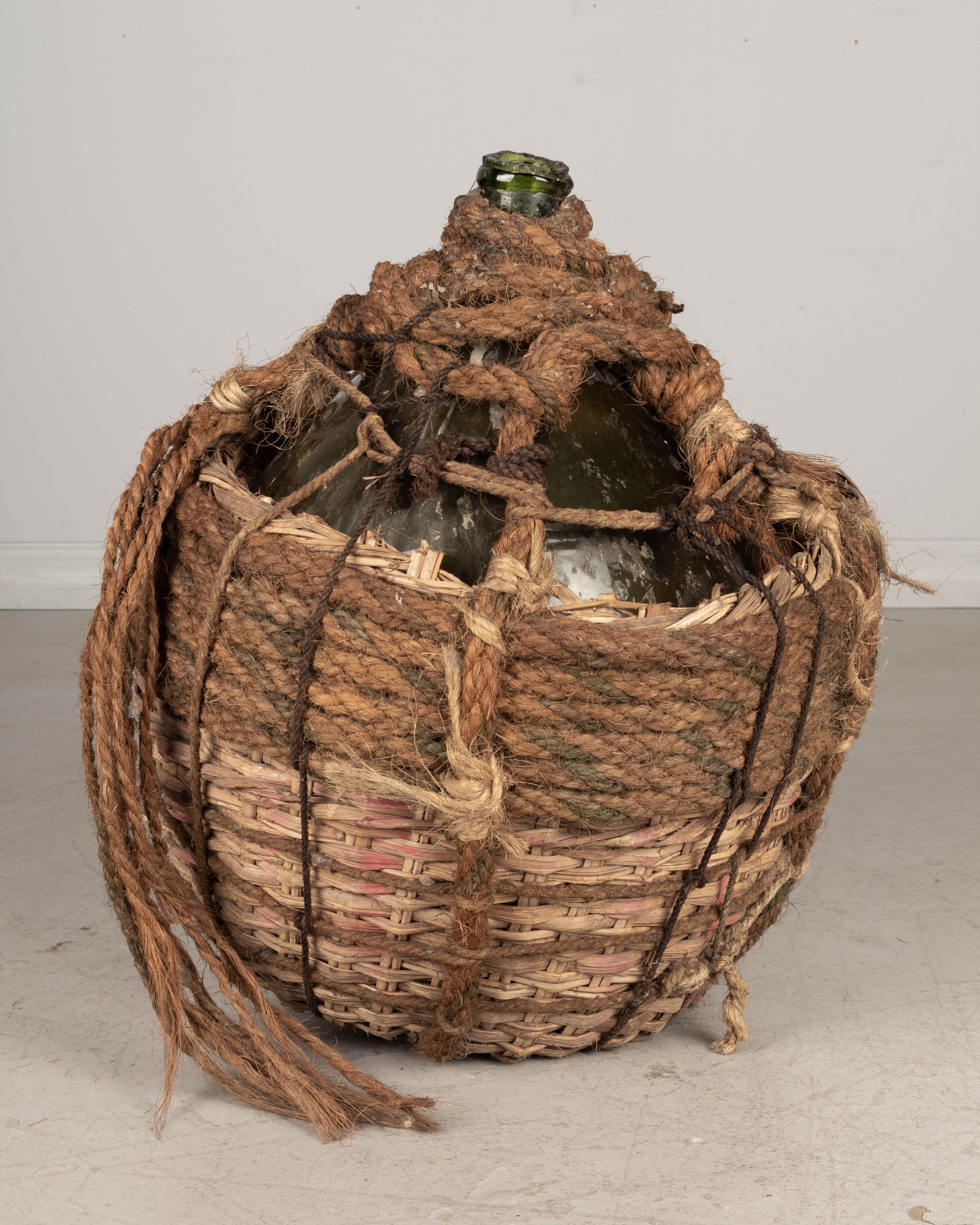 A large 19th century French globular form hand blown green glass Dame Jeanne, or demijohn, bottle encased in two layers of woven wicker and thick braided rope. Layers of different kinds of rope appear to have been added over the years creating an