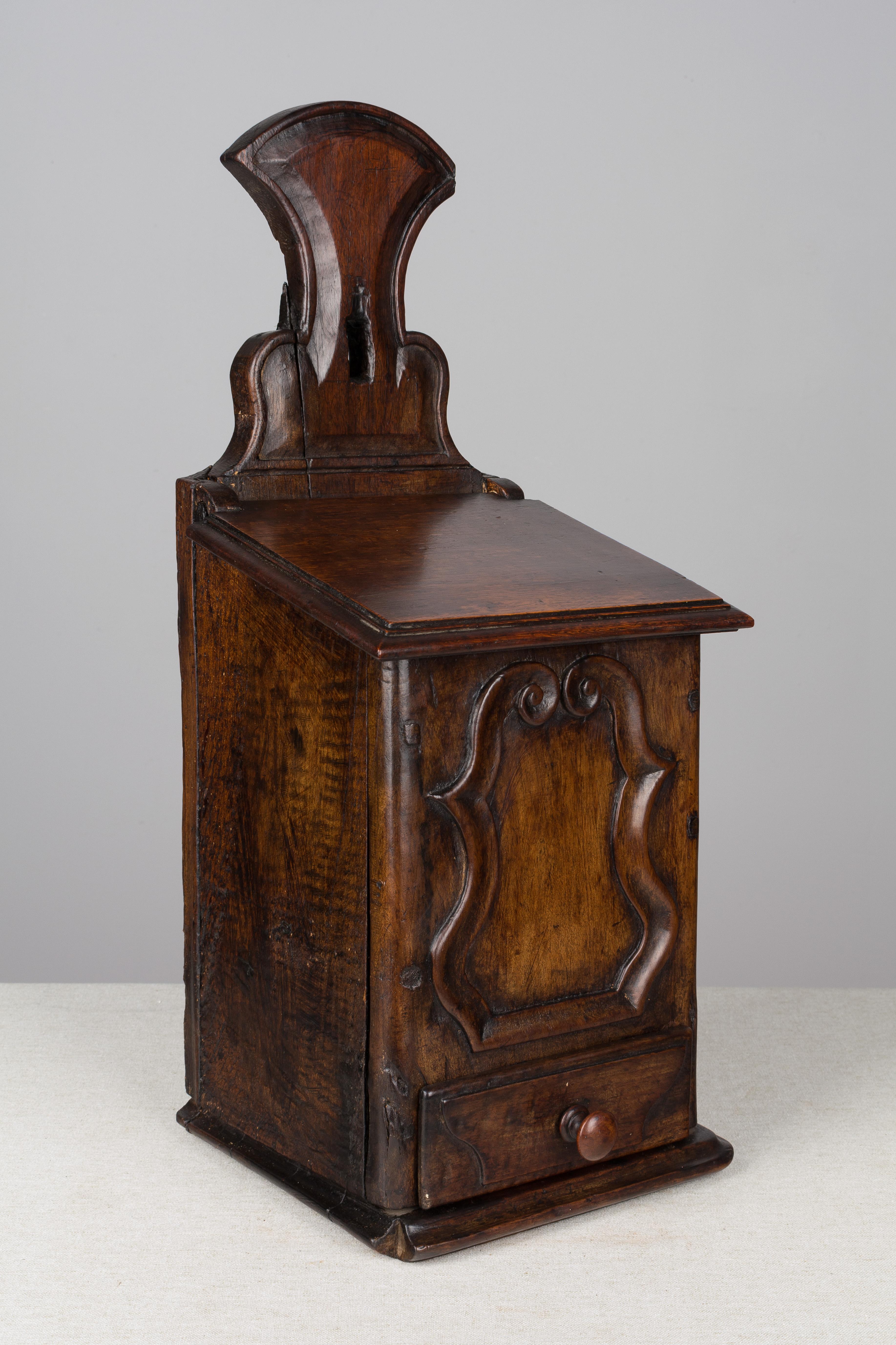 An early 19th century French boite à sel, or salt box, made of walnut with hinged lid and small drawer with turned knob. Bold hand-carved decoration. Waxed finish. Unusually large size. In very good condition with two minor losses. This box was used