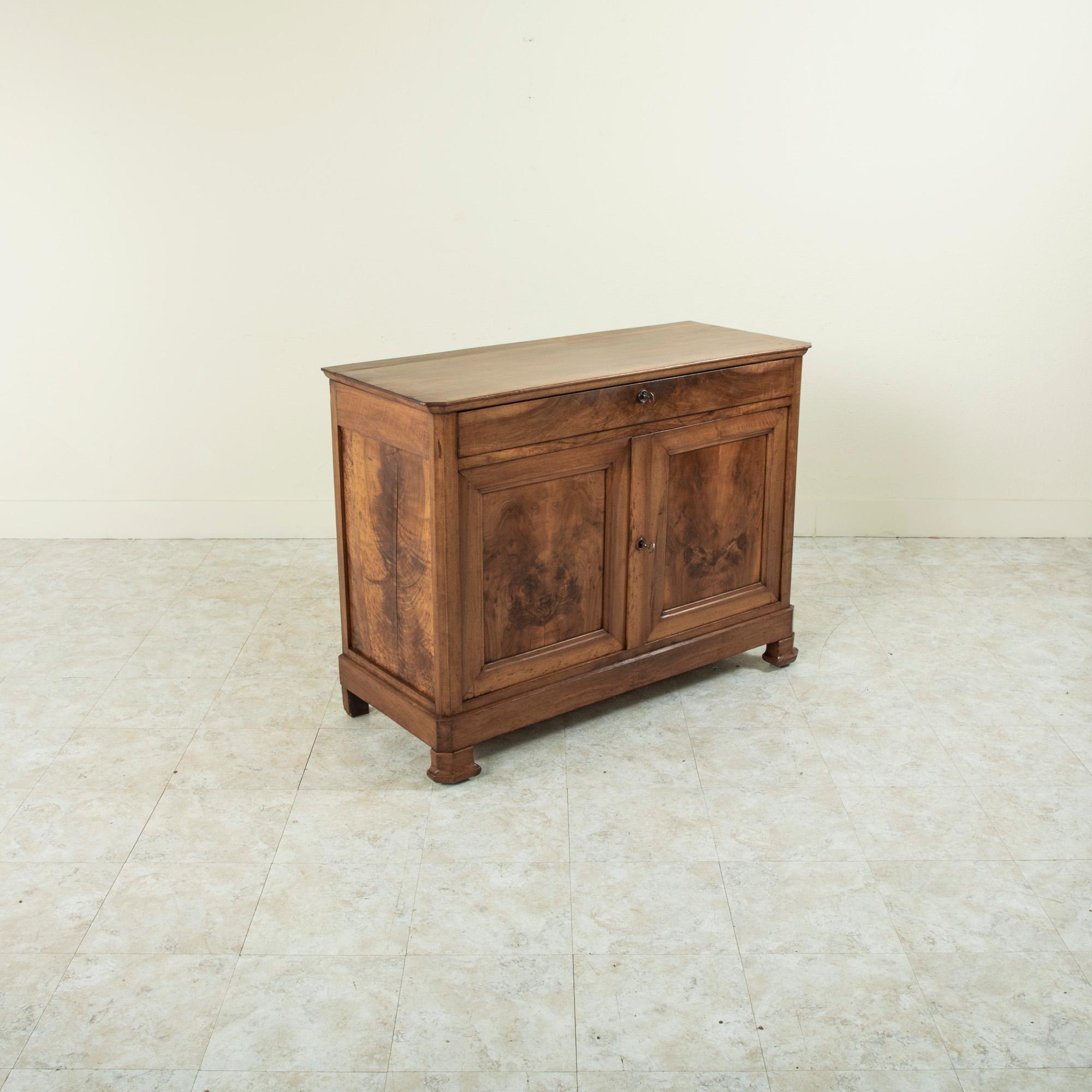 With only a 46.5 inch width, this small scale Louis Philippe period buffet from the nineteenth century is constructed of solid walnut. It features a single drawer of dovetail construction that fits seamlessly into the apron and two book matched
