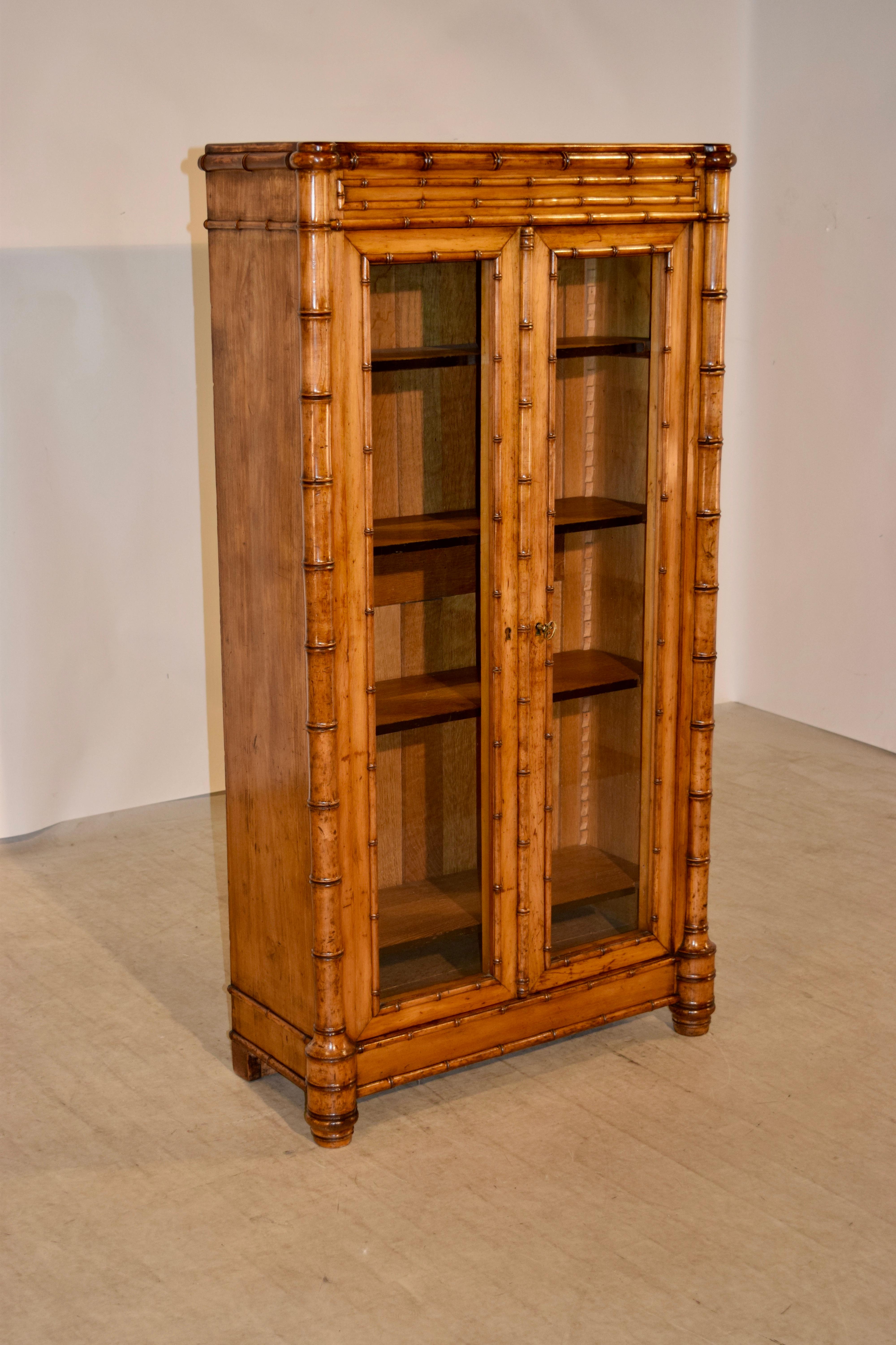 19th century bookcase from France made of cherry with simple sides embellished with faux bamboo turned moldings and round faux bamboo turned columns on the front corners which end in interesting hand-turned graduated feet, also hand-turned in the