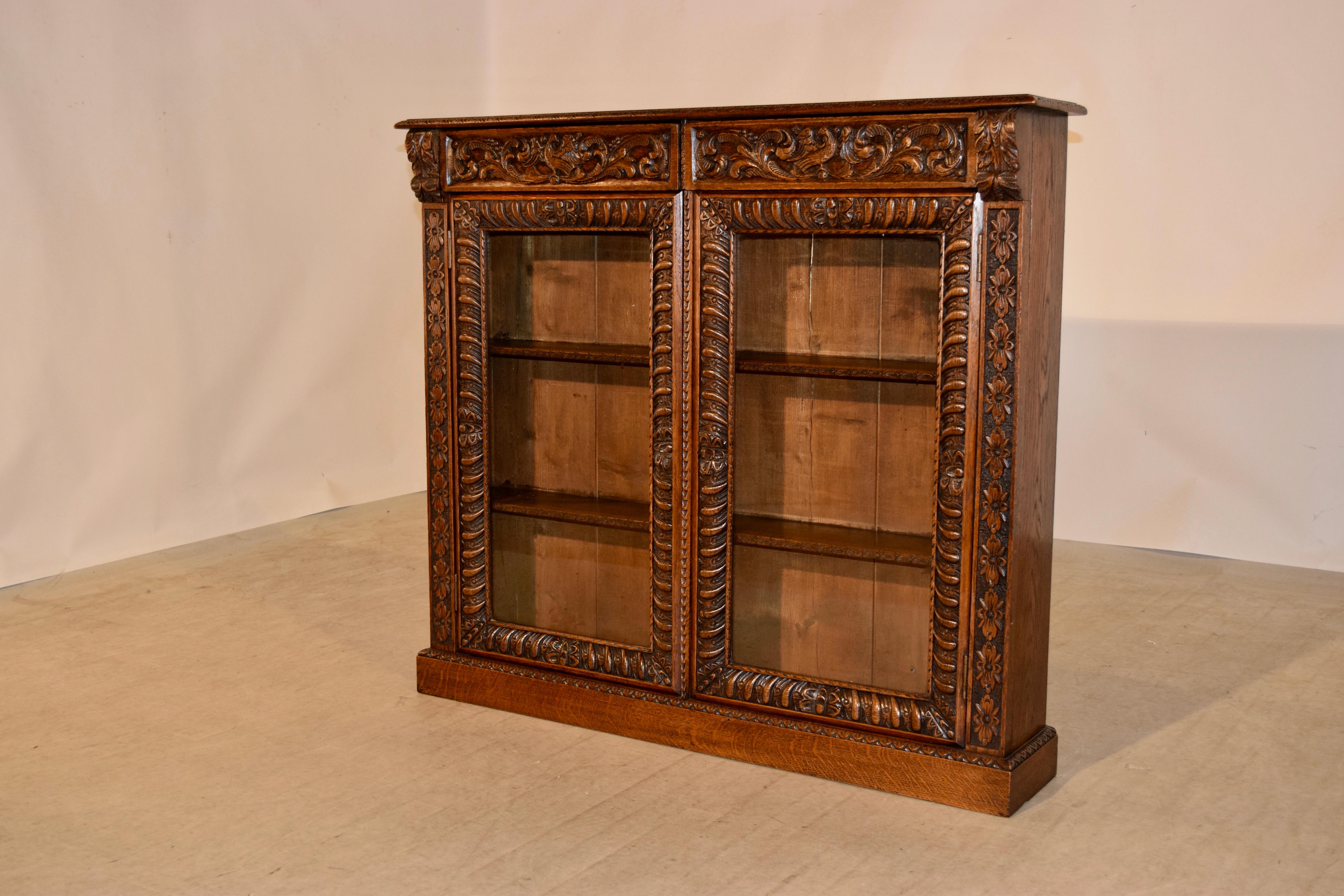 19th century French bookcase made from oak with a beveled and gadrooned edge following down to two drawers, which are wonderfully hand carved decorated over two glazed doors with hand carved framing. Flanked by hand carved side columns. The doors