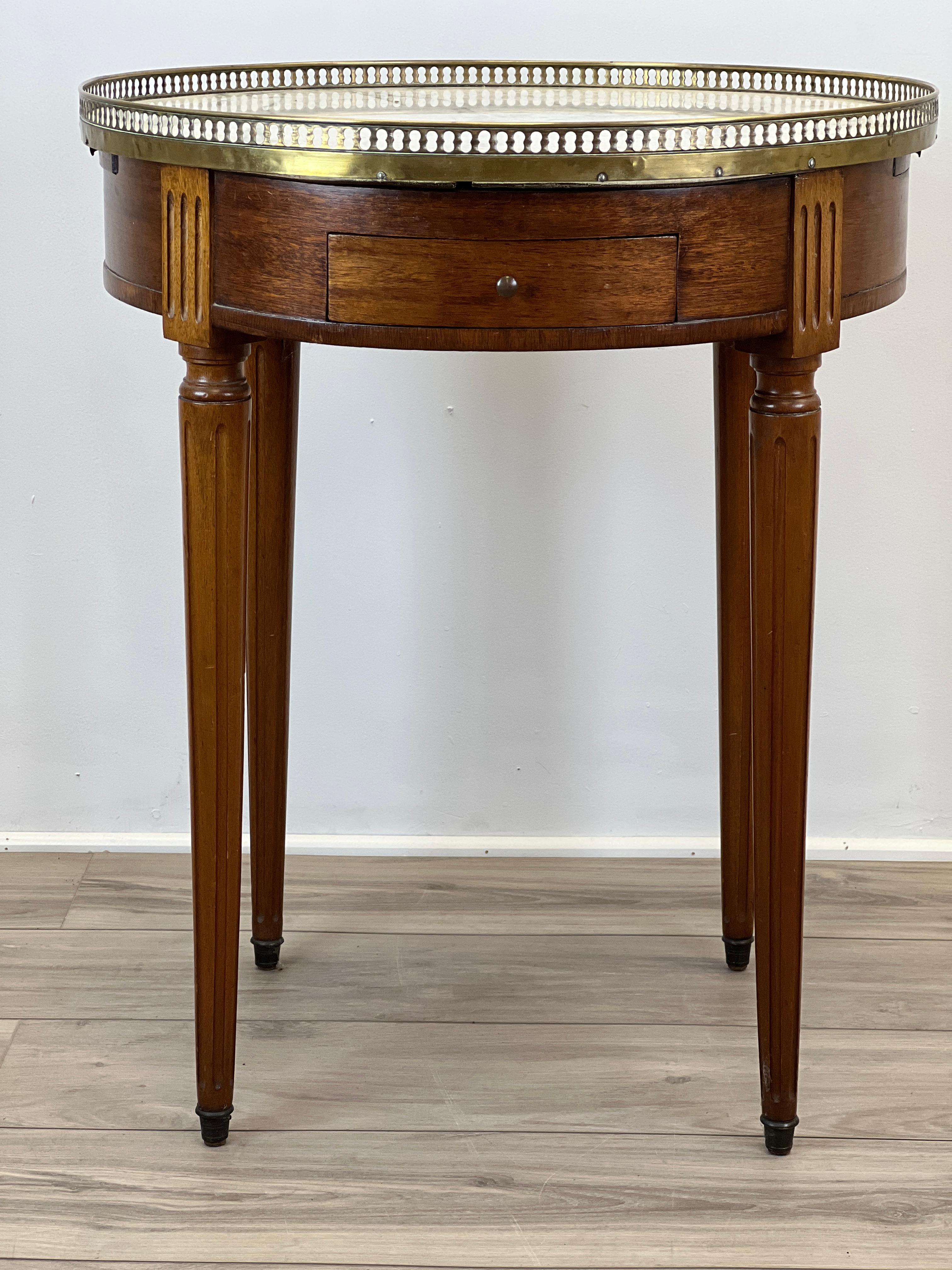 This is a late 19th century French Bouillotte table made from Mahogany and Oak. The top is made of white marble with a brass gallery perimeter in the traditional style. There are two drawers front and rear with hand cut dovetail joints. There are