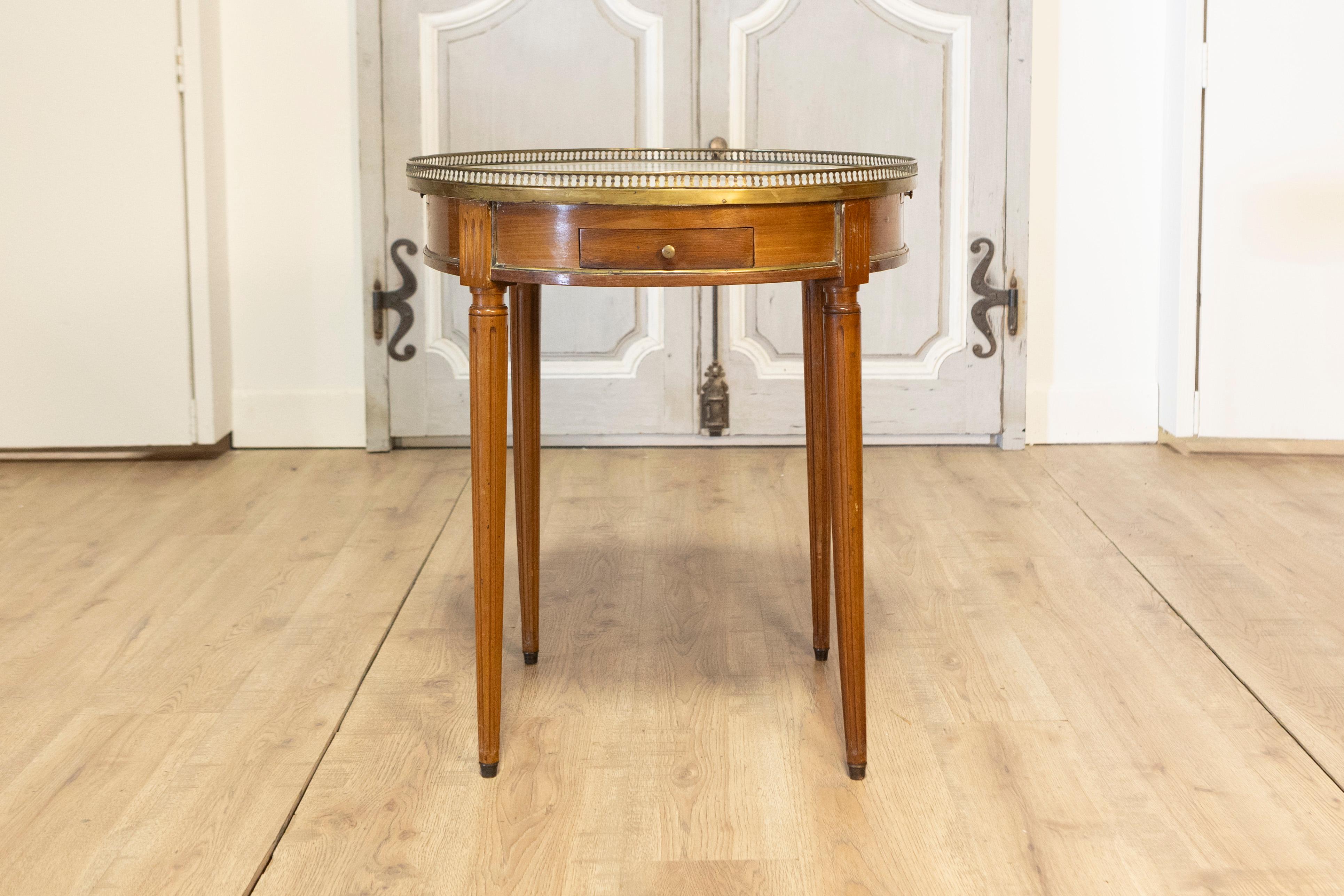 Une table Bouillotte française raffinée du XIXe siècle, qui témoigne de l'élégance et du savoir-faire du style Louis XVI. Cette table circulaire présente un plateau en marbre blanc entouré d'une galerie en laiton percée, ajoutant une touche