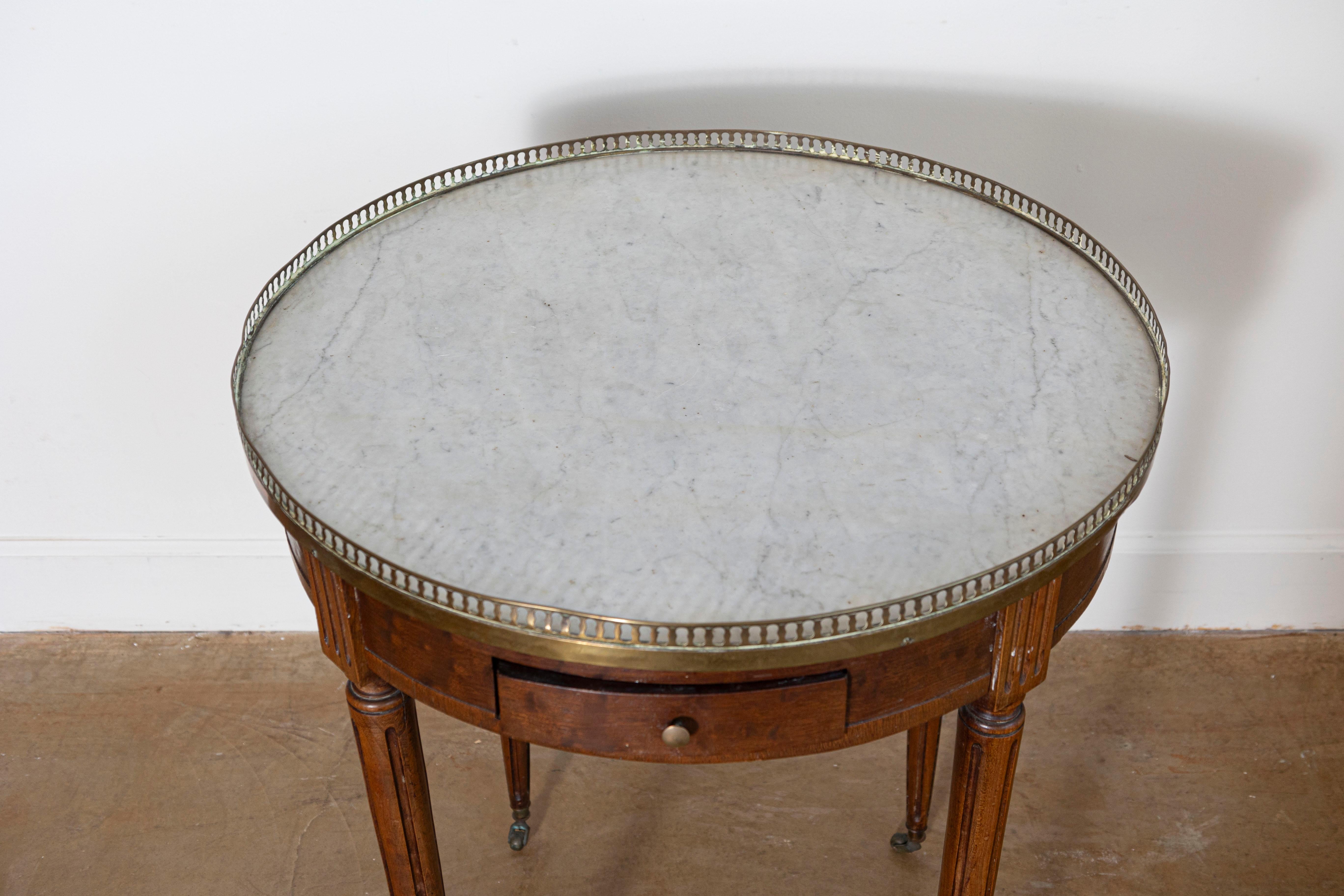 Esta mesa Bouillotte francesa del siglo XIX muestra la elegancia y funcionalidad características del diseño neoclásico. Fabricada en caoba, la mesa presenta un tablero redondo de mármol rodeado por una galería de latón perforado, que añade un toque