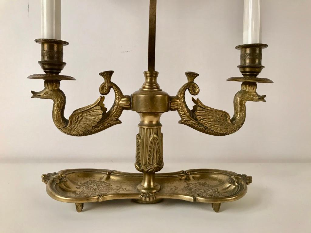 Bronze two light bouillotte lamp with swam form arms and green painted metal shade with floral gilt border. The unusual kidney shaped base with incised decoration, French, circa 1890.

Bouillotte is an 18th century French gambling card game of the