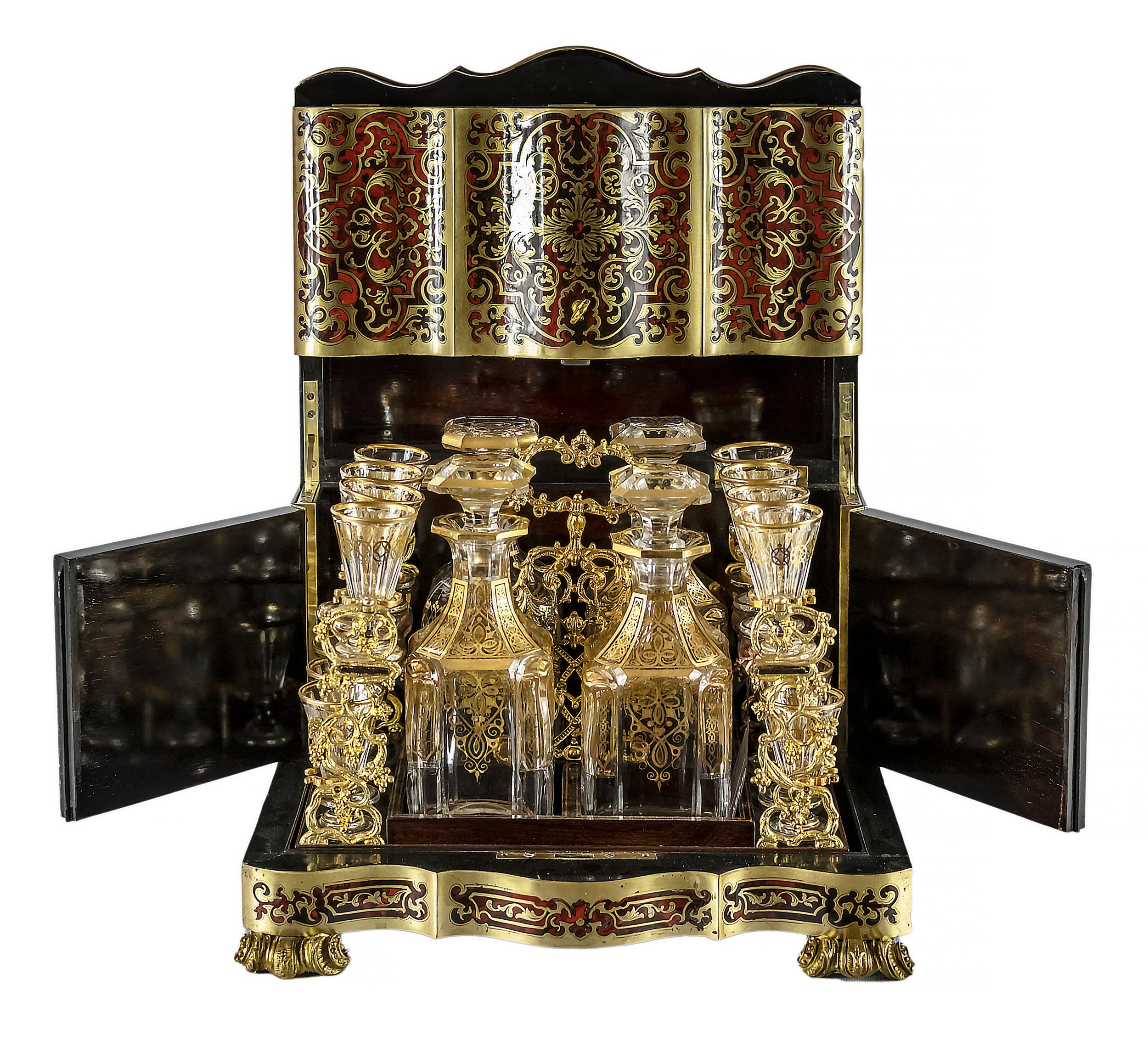 Antique French liqueur cave box with inlaid brass and and tortoise shell marquetry decor, a lift top door and swing side doors, polished surface, bronze legs.
Inside there is a wooden and bronze holder with four 4 crystal carafes and 16