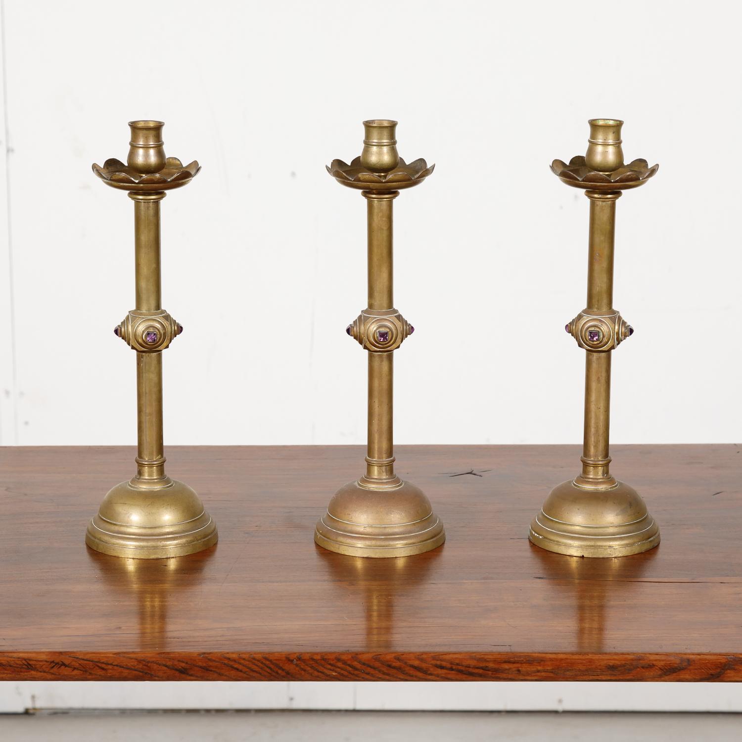 Beautiful set of three 19th century French solid brass classic style altar candlesticks from a church in the South of France near Arles, each having four square shaped inset cabochon amethysts and all are surmounted by a wide circular drip tray,