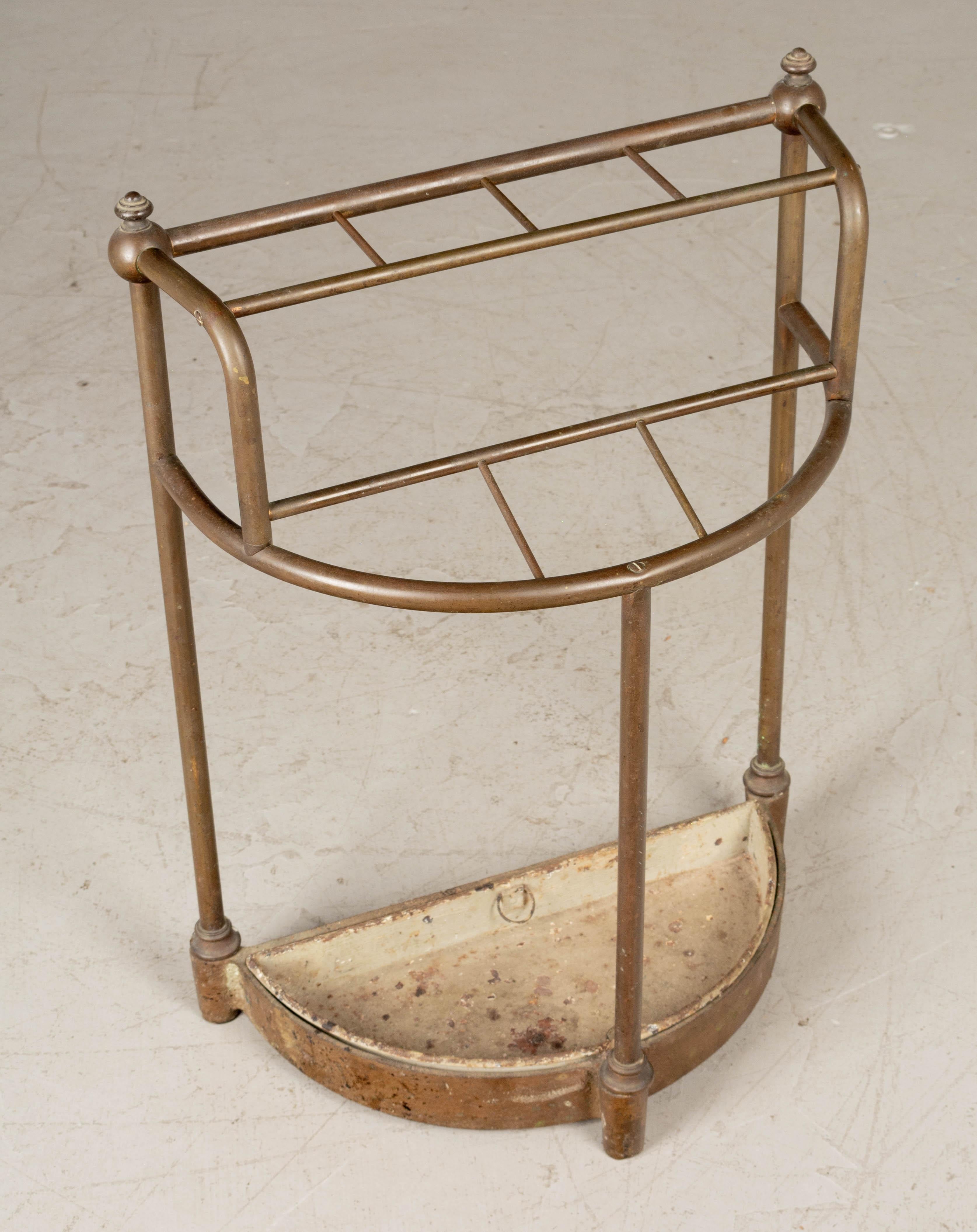A 19th century French brass and cast iron umbrella stand. Demilune form with brass tubing and decorative finials. Cast iron base with removable drip tray. 
More photos available upon request. We have a large selection of French antiques. Please