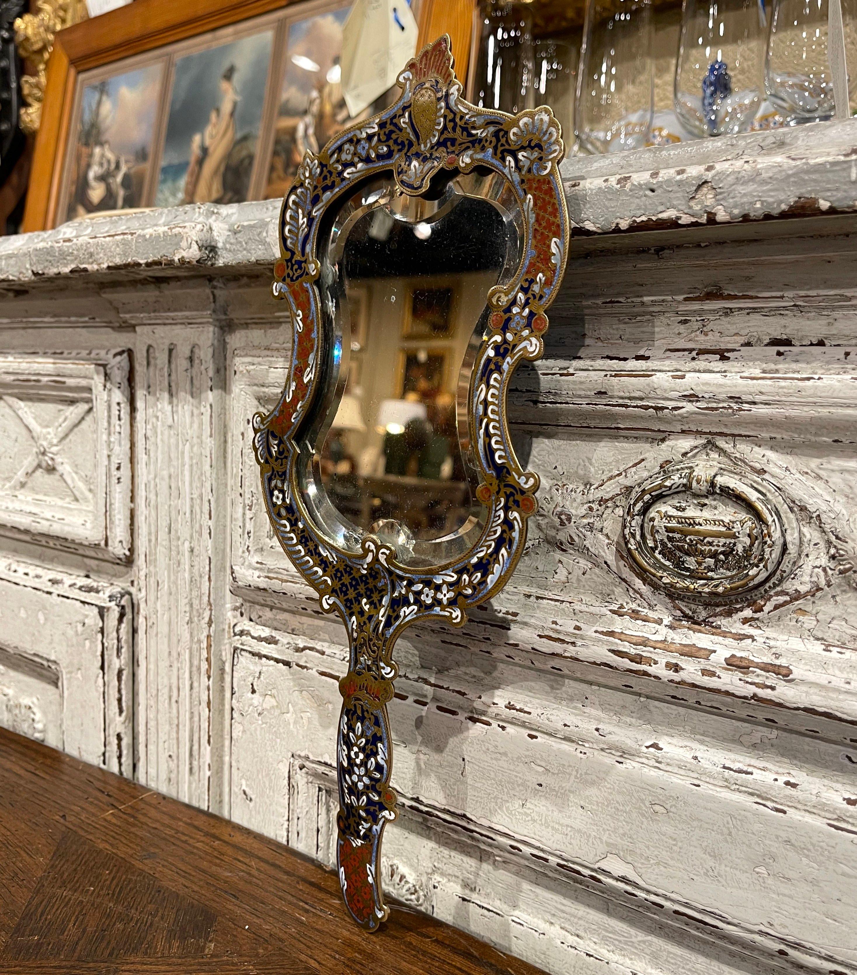 Crafted in France circa 1870, the colorful antique Louis XV hand mirror features elegant and intricate cloisonné decor throughout; it is further dressed with an inset beveled glass. The decorative vanity mirror is in excellent condition with bright