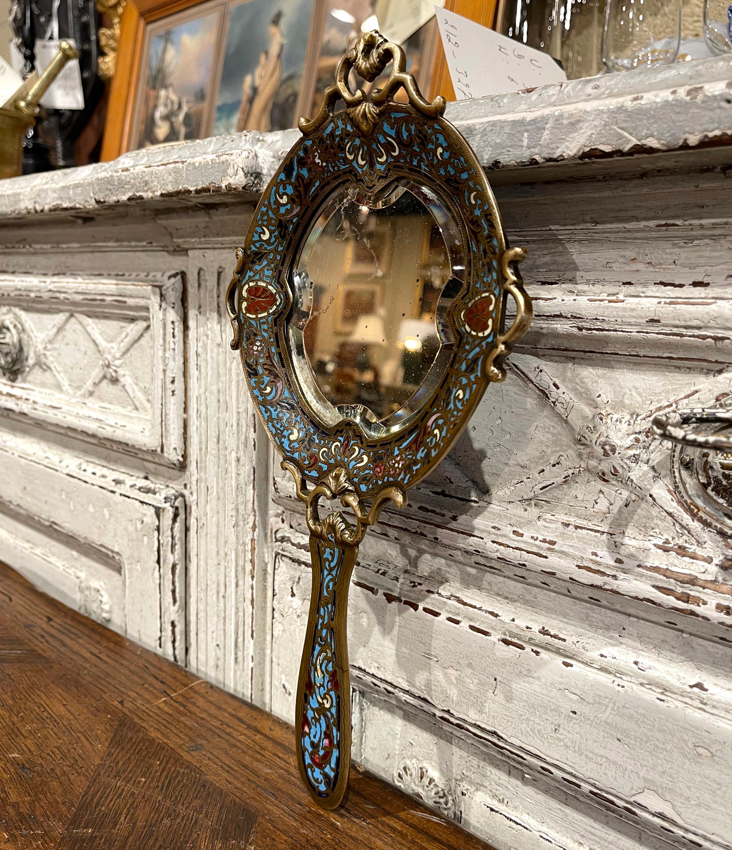 Crafted in France circa 1870, the colorful antique Louis XV hand mirror features elegant and intricate cloisonné decor throughout; it is further dressed with an inset beveled glass. The decorative vanity mirror is in excellent condition with bright