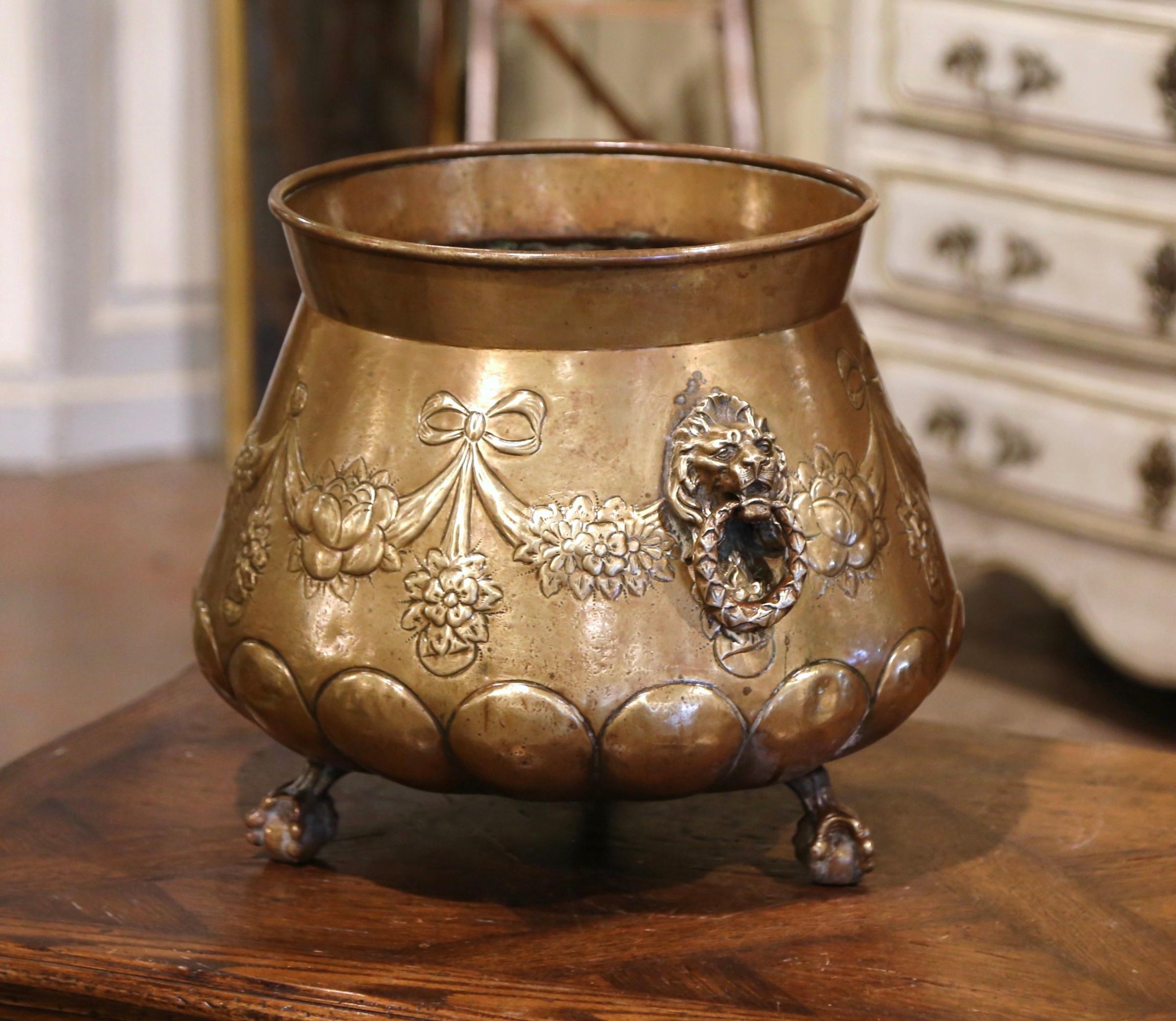 This large brass planter was crafted in France, circa 1880. Round in shape, the decorative cache pot stands on small paw feet and features intricate repousse decor with floral and swag motifs embellished with lion heads figures handles. The large