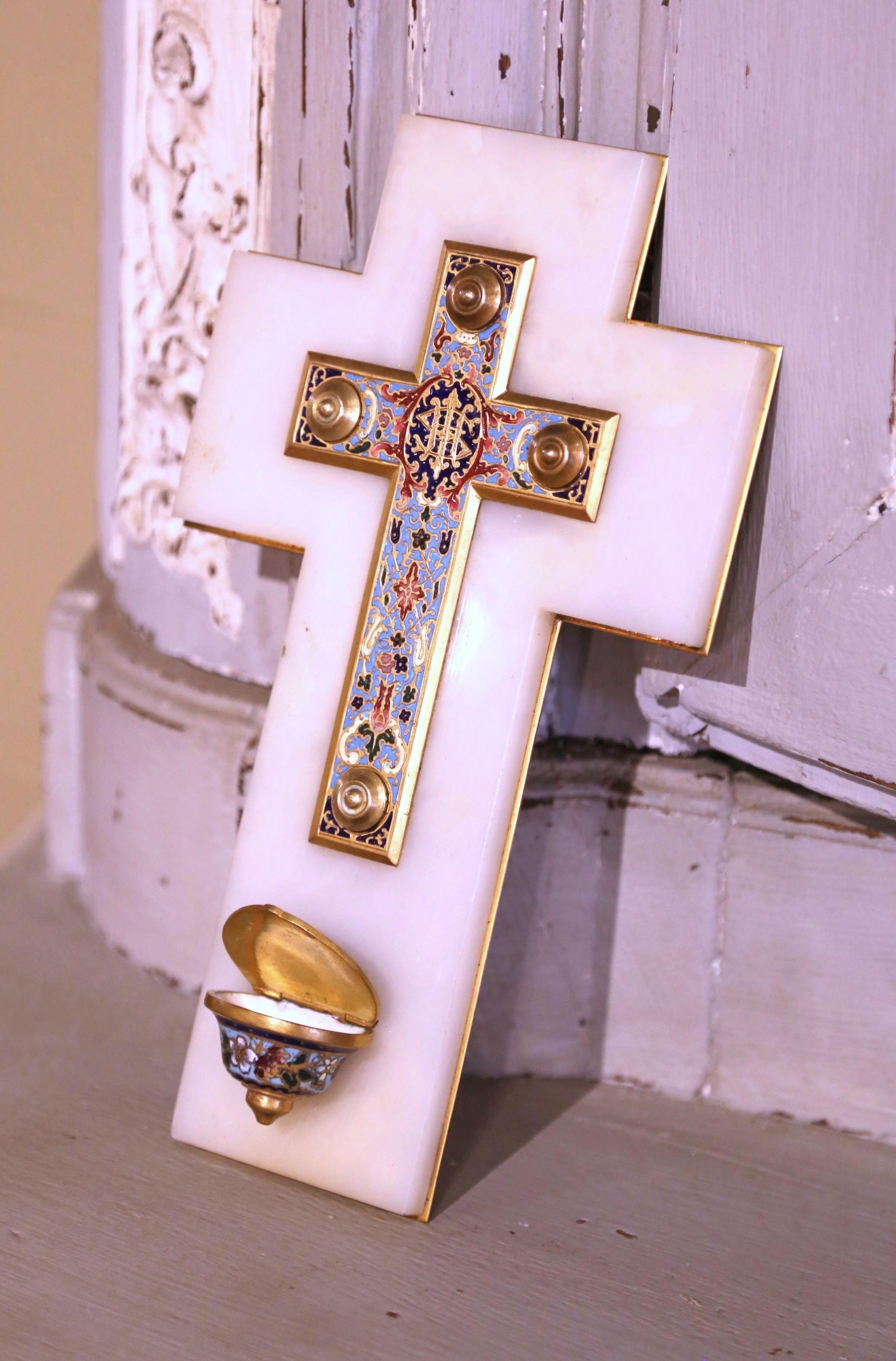 Améliorez votre espace de dévotion avec ce bénitier français ancien et coloré, fabriqué vers 1880. Posé sur une base en marbre blanc en forme de croix, le centre de la pièce présente un crucifix en émail champlevé richement décoré de motifs floraux