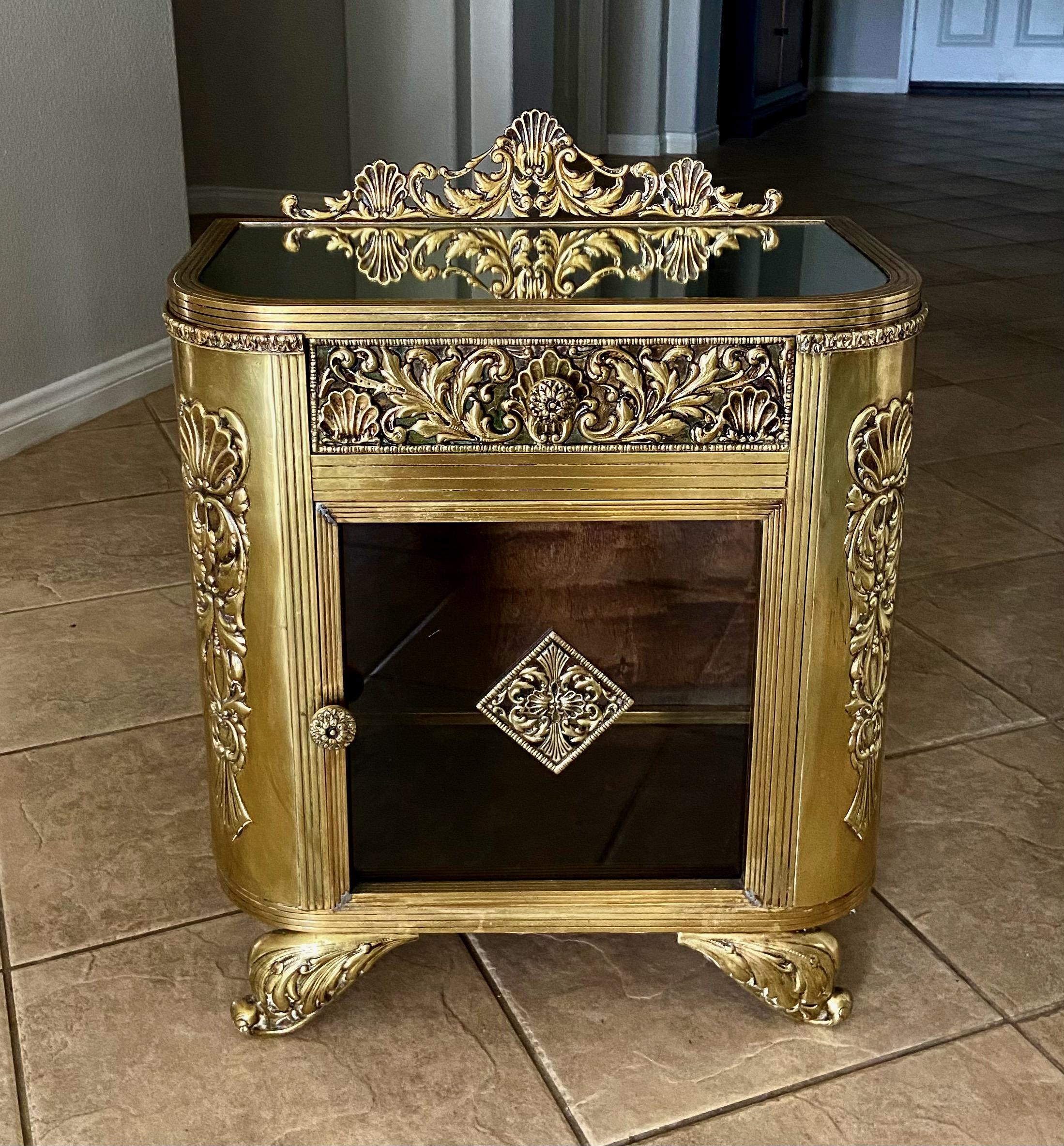A unique smaller scale French antique brass cabinet with 1 door and 1 pull out drawer. The outer brass cabinet is expertly crafted with filigree elements throughout. The front cabinet door has clear glass with floating brass element in center, each
