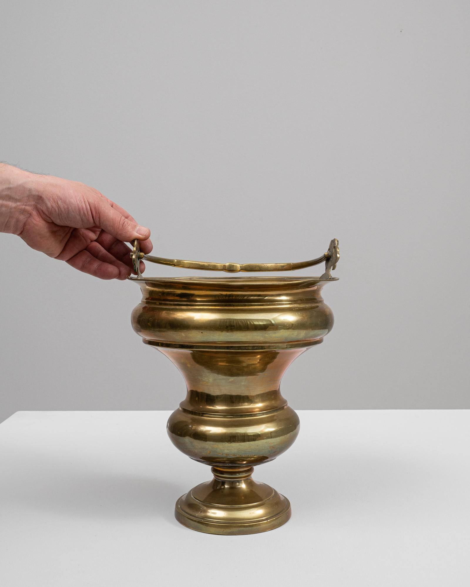 This 19th-century French brass ice bucket is a marvelous relic of elegance. Crafted from lustrous brass, it features a classic silhouette with a banded design adding a touch of sophistication to its shape. The gracefully arched handle is secured by