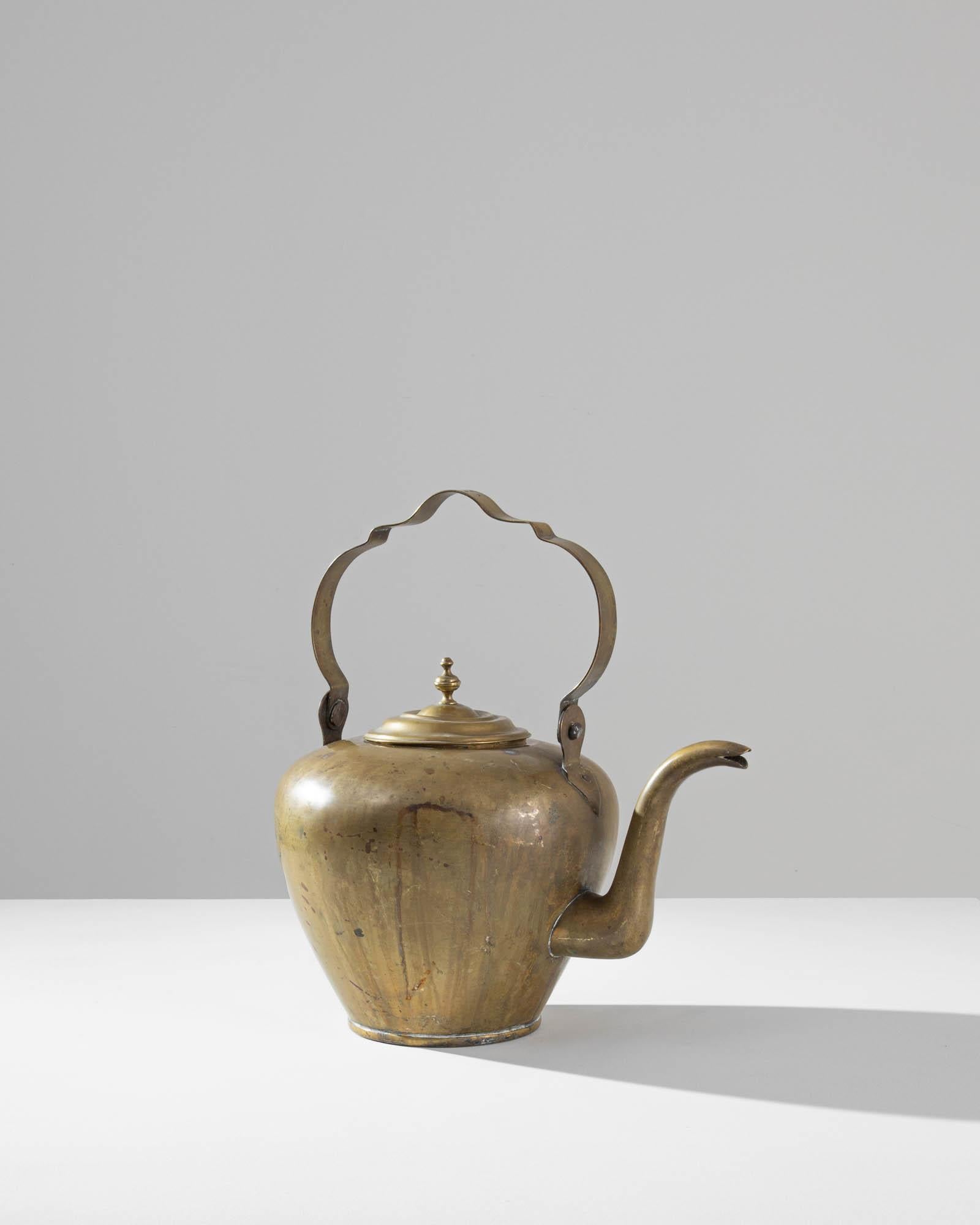 This elegant antique tea kettle makes a delightful addition to a kitchen. Made in France in the 1800s, the shape of the tall handle indicates that this piece would have originally been hung over a fire. Little details of the design—the graceful