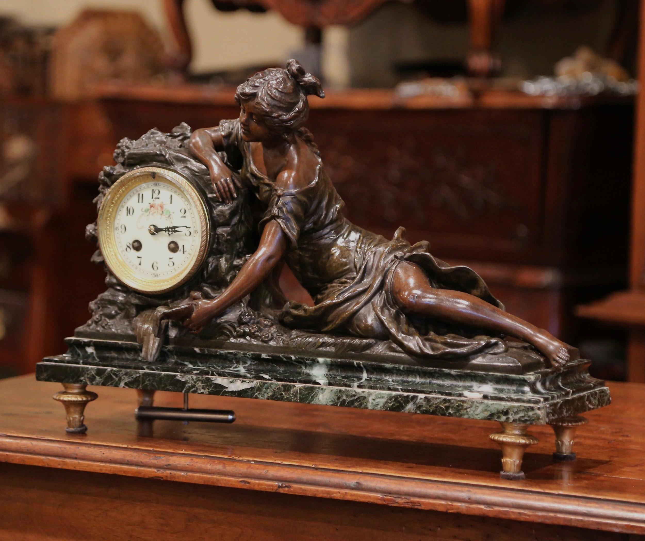 This elegant mantel clock was created in France circa 1860. The asymmetrical bronze clock signed L & F Moreau, sits on a marble base with small feet at the bottom. The clock top features a woman sculpture lying down and pouring wine. The female