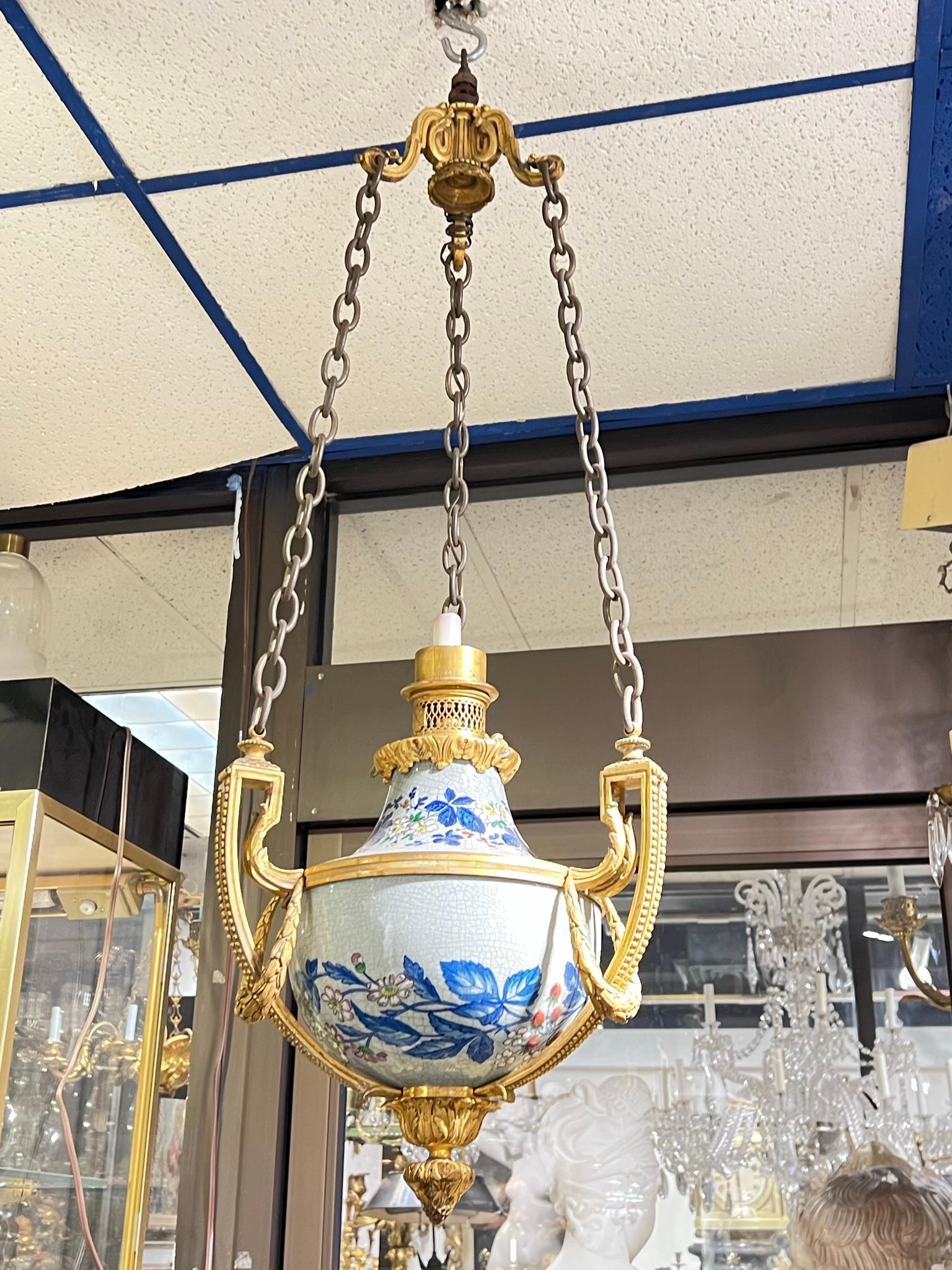 Unique 19th century hanging oil lamp by Gagneau and Company of Paris, with urn form crafted from faience with blue, red and pink flowers and leaves on a cream colored ground, with neoclassical gilt bronze mounts and suspended from three chains. 